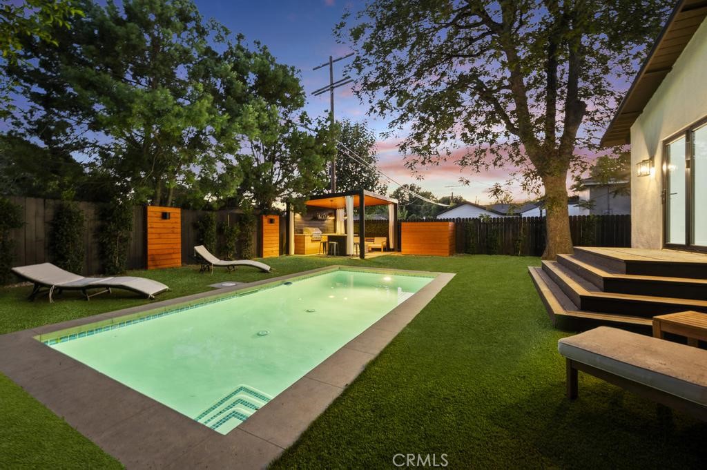 Tucked away on a lush, tree-filled lot, this modern retreat offers the perfect balance of privacy and resort-style living. A remote-controlled iron gate opens to reveal a beautifully reimagined 5-bedroom, 4-bathroom home showcasing timeless design and high-end upgrades throughout. Inside, the open-concept floor plan is anchored by White Oak hardwood floors and a sleek designer kitchen with quartz countertops, under-lit cabinetry, matching Thor appliances, and a built-in three-temperature wine refrigerator. The expansive primary suite overlooks the serene backyard and features a spacious walk-in closet along with a spa-inspired ensuite highlighted by dual sinks and a curb-less, zero-entry shower. Three additional designer bathrooms echo the same attention to detail with walk-in showers and luxury finishes. Step outside to your private paradise: a brand-new sparkling pool shaded by mature trees and complemented by a resort-style cabana. Designed for entertaining, the cabana is complete with an outdoor kitchen, built-in Spires BBQ, dual-temperature wine fridge, mounted TV, overhead lighting, and a cozy fire pit. Recent upgrades provide peace of mind, including a new roof, HVAC system, water heater, all-new copper and PEX plumbing, smooth stucco exterior, stamped concrete driveway, and low-maintenance synthetic turf in both the front and back yards. A rare blend of sophistication, comfort, and modern California living, this home is a true retreat designed for both relaxation and entertaining.