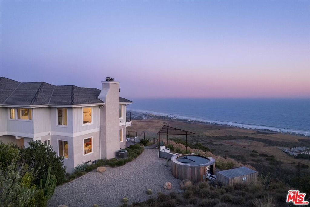 Set high above the Pacific on 3.28 private acres, this stunning Malibu coastal retreat offers unobstructed vistas spanning Zuma Beach, the Santa Monica Mountains, Point Dume, Catalina, and the Channel Islands. Merging privacy, scale, and refined architecture, this property represents a rare opportunity just moments from Broad Beach and Vintage Grocers. Crafted to showcase its spectacular surroundings, the residence embraces a modern coastal aesthetic defined by clean, elegant lines and seamless indoor-outdoor living. The expansive great room features wraparound ocean views, Italian oak floors, and a striking sculptural stone fireplace. Floor-to-ceiling pocket doors dissolve boundaries, opening onto a sweeping entertaining terrace perched above the bluff. Beyond the main terrace, an ocean-facing deck provides dedicated spaces for dining and lounging, thoughtfully positioned to capture the evolving coastal light from dawn until dusk. The chef's kitchen impresses with marble countertops, premium appliances, a full butler's pantry, and a sun-filled breakfast nook opening onto the deck. Additional living spaces include a den with an adjoining an ocean-view office with a private balcony. Upstairs, the luxurious primary suite boasts a private terrace with panoramic views, fireplace, sitting area, dual walk-in closets, and an expansive ensuite bath. Three additional bedrooms offer diverse perspectives of the coastline, mountains, and gardens. The beautifully landscaped grounds unfold in tranquil layers: a bluff-top lounge deck, meticulously terraced native plantings, a serene Japanese soaking spa paired with a sunken conversation pit, and a charming boardwalk pathway leading to a secluded sandy retreat. Additional highlights include a three-car garage complete with a gym and laundry area, a private well with storage tanks, and fully fenced grounds. 6007 Trancas Canyon embodies a rare harmony of thoughtful design and the breathtaking natural beauty of Malibu's iconic coastline.