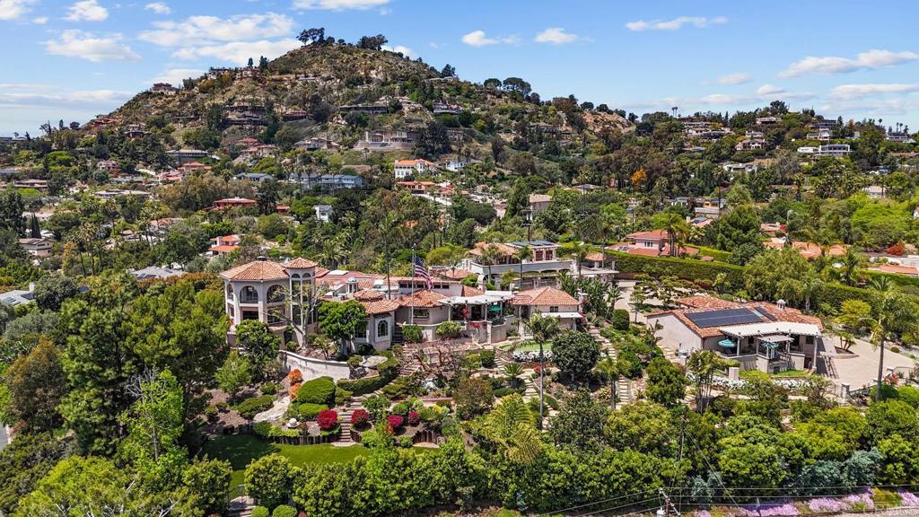 Discover an unparalleled opportunity in Mt. Helix with this expansive 2.41-acre estate, comprising a 5,872-sq-ft Santa Barbara–inspired main residence, a 2,428-sq-ft meticulously remodeled casita and a separate 0.77-acre ready-to-build vacant lot. The main residence blends architectural elegance with resort-style amenities, featuring interconnected octagonal structures and a dramatic tower room offering 360° panoramic views. Formal and casual living areas complement a chef’s kitchen and a primary suite that opens to a wraparound terrace. An executive office adds functionality, while the lower level includes versatile bedrooms, auxiliary flex rooms, and a gym/storage space. Outdoors, botanical gardens with over 100 rose varieties, four tranquil fountains, and diverse specimen trees create a serene setting. Multiple pools and spas, including an elevated spa with sweeping views to the east, south, and west—encompassing Downtown San Diego and Point Loma—provide relaxation, while expansive terraces and a fully equipped outdoor kitchen enhance alfresco dining experiences. Centrally located between the pools, a two-story pool house features multiple bathrooms, a rejuvenating sauna, and the “Las Brisas” guest retreat with a detached gym/yoga studio and direct spa access. The casita, extensively renovated in 2018, offers a chef’s kitchen, hardwood floors, exposed wood beam ceilings, and a separate downstairs studio with a full bath and kitchenette. Completing this exceptional estate is a generous buildable lot equipped with a private water well currently used for irrigation, offering sustainable landscaping and potential for future development or added privacy. This estate masterfully combines architectural elegance, luxurious amenities, and breathtaking views, offering a one-of-a-kind living experience in the prestigious Mt. Helix community.