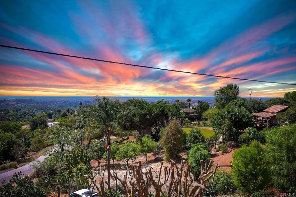 Welcome to your private hilltop retreat in Vista’s scenic Elevado Hills! Tucked away on the shared private road of Aloha Lane, this beautifully landscaped property offers nearly one acre of fully fenced land with dual gated entry for easy ingress & egress. Enjoy breathtaking panoramic views of the ocean, mountains, valleys, city lights, sunsets, & seasonal fireworks from the expansive ~1,250 sq. ft. custom view deck—an entertainer’s dream! The deck flows effortlessly from the spacious living room with a wet bar, fireplace-warmed dining room, & an open-concept kitchen featuring an island & walk-in pantry. This sprawling single-story ranch home features 3 bedrooms in the main residence, including 2 with direct bathroom access, & a 4th private bedroom & full bath located off the back side of the attached 2-car garage—ideal for guests, home office, or multigenerational living. A second detached 2-car garage/workshop, complete with air compressor, is perfect for hobbyists or car enthusiasts The lush, mature landscaping includes citrus trees, macadamia nut trees, & more, creating a peaceful, park-like setting with room to grow. Located in one of Vista’s most sought-after neighborhoods, you’re just minutes from Moonlight Amphitheater, excellent dining, shopping, & wineries, golf courses, hiking, & beaches, plus quick access to highways 76, 78, 5, & 15. Recent upgrades include mostly newer plumbing, brand new septic tanks, Section 1 termite clearance, & available property inspections & seller disclosures for peace of mind. This is more than a home—it’s a lifestyle. Come experience the magic of Elevado Hills!
