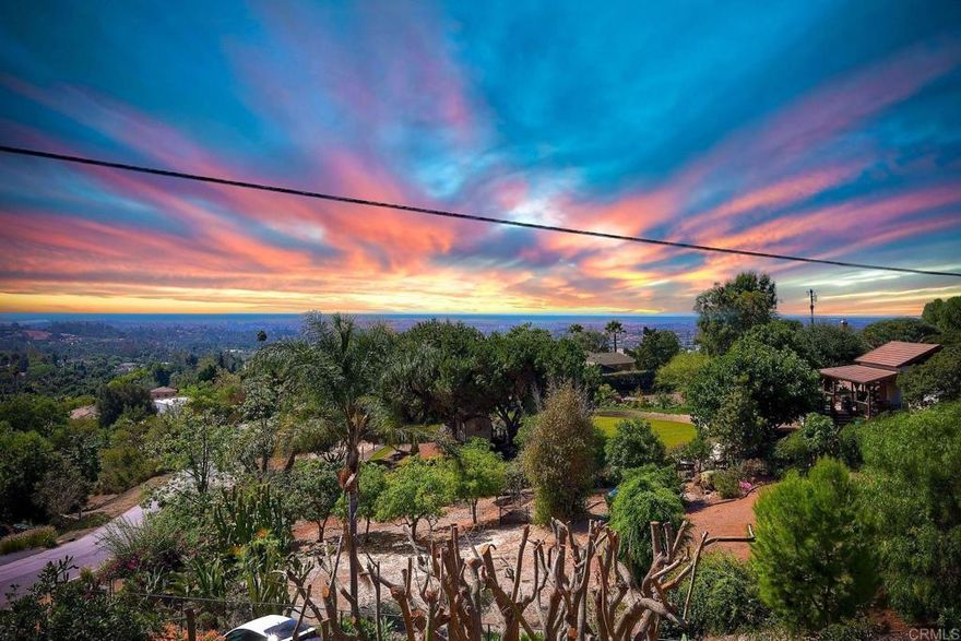Welcome to your private hilltop retreat in Vista’s scenic Elevado Hills! Tucked away on the shared private road of Aloha Lane, this beautifully landscaped property offers nearly one acre of fully fenced land with dual gated entry for easy ingress & egress.  Enjoy breathtaking panoramic views of the ocean, mountains, valleys, city lights, sunsets, & seasonal fireworks from the expansive ~1,250 sq. ft. custom view deck—an entertainer’s dream! The deck flows effortlessly from the spacious living room with a wet bar, fireplace-warmed dining room, & an open-concept kitchen featuring an island & walk-in pantry.  This sprawling single-story ranch home features 3 bedrooms in the main residence, including 2 with direct bathroom access, & a 4th private bedroom & full bath located off the back side of the attached 2-car garage—ideal for guests, home office, or multigenerational living. A second detached 2-car garage/workshop, complete with air compressor, is perfect for hobbyists or car enthusiasts  The lush, mature landscaping includes citrus trees, macadamia nut trees, & more, creating a peaceful, park-like setting with room to grow.  Located in one of Vista’s most sought-after neighborhoods, you’re just minutes from Moonlight Amphitheater, excellent dining, shopping, & wineries, golf courses, hiking, & beaches, plus quick access to highways 76, 78, 5, & 15.  Recent upgrades include mostly newer plumbing, brand new septic tanks, Section 1 termite clearance, & available property inspections & seller disclosures for peace of mind.  This is more than a home—it’s a lifestyle. Come experience the magic of Elevado Hills!