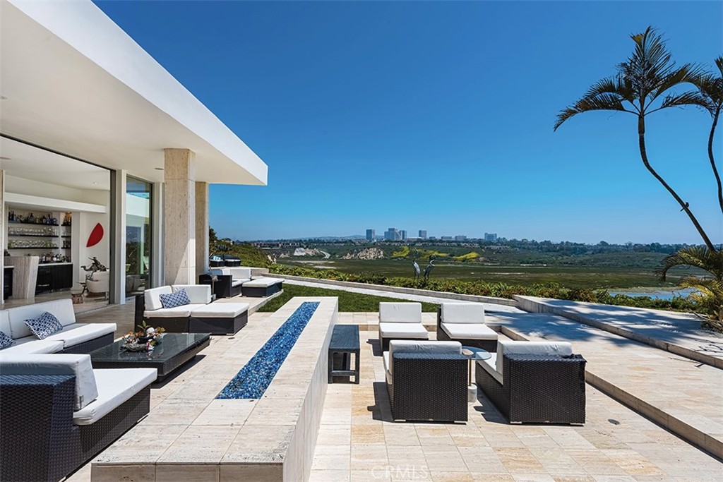 Poised above the prestigious bluff of Dover Shores with extraordinary views of Newport’s Back Bay and the Pacific coastline, 1336 Galaxy Drive is a masterwork of architecture and artistry. Originally designed in 1963 by renowned Los Angeles architect Harold Levitt for Virginia Knott Bender, this estate has been reimagined into a Mediterranean Modern sanctuary, blending open-plan design with coastal resort living.
Spanning nearly 5,000 square feet, this residence includes a statement-making 6’ x 9’ glass entry door with offset pivot hardware that opens up to a private courtyard which enhances privacy while connecting the spaces to a fully integrated smart home that elevates the experience of indoor-outdoor living. The second gateway controlled by a pair of 14’ high Herculite® double glass doors opens into a pool atrium space with open-concept living areas featuring floor-to-ceiling retractable glass doors, a retractable translucent roof, custom-cut travertine flooring, and a design aesthetic that reflects California's contemporary style, evoking serenity and inspiration. The four en-suite bedrooms — three of which open directly to the pool atrium — are generous in size and accentuated by high 9’ plate ceilings, while the primary suite offers a private sanctuary with direct views of the Back Bay. The primary suite features a gas fireplace, a luxurious bath with refined finishes, and a bespoke walk-in wardrobe. Additional highlights include a stylish home office, a versatile room that can serve as a bedroom or gym, a full laundry suite, and expansive outdoor spaces designed for entertaining.
The chef’s kitchen is a celebration of function and form, featuring top-tier Thermador, Dacor, Asko, and Gaggenau appliances, including a built-in steamer and teppanyaki stations. The kitchen flows seamlessly into the pool atrium, offering effortless indoor-outdoor entertaining beneath the ever-changing sky.
Outdoor spaces invite both contemplation and celebration, featuring a Back Bay-view fire lounge, LED-lit bocce court, al fresco dining terrace, surf shower with board storage, EV charger, and a dedicated gear/storage garage.
Crafted with passion over five visionary renovation phases (2010–2025), 1336 Galaxy Drive is more than a home—it is an experience shaped by its stunning views, architecture, setting, and breathtaking design.