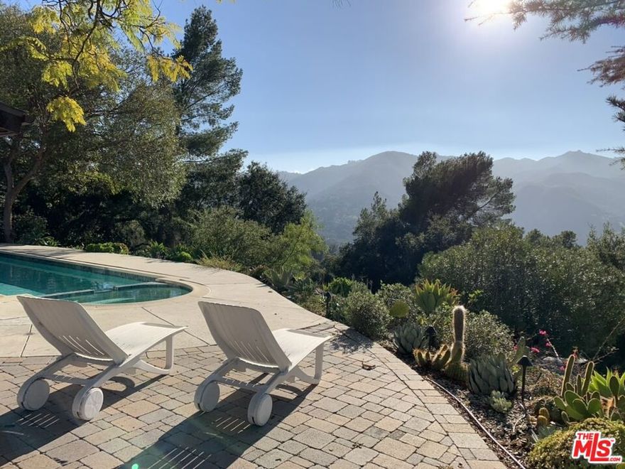 Original Mid-Century Architectural Topanga Pool Home with expansive views by architect Bob Bates. Perched high above the canyon on a serene knoll in the coveted Pos Office Tract, this original Mid-Century architectural home stands as a luminous ode to Topanga's artistic spirit. The essence of Frank Lloyd Wright's Honeycomb House lives on here. Tucked up a private driveway that meanders beside the State Park, the property opens to a world of quiet grandeur, a landscape of golden light, rustling oaks, and boundless vistas that seem to float between earth and sky. Here, architecture and nature entwine in a lyrical balance, every beam and pane of glass choreographing the movement of sunlight across redwood walls, wood floors, and polished stone floors. Inside, the home unfolds with the understated drama of true mid-century design, post-and-beam vaulted ceilings, crisp white walls, and generous expanses of glass that dissolve the boundary between indoors and out. The living room, centered around its original, rugged stone, wood-burning fireplace, feels suspended in air, gazing out over the lap pool and hot tub to views that stretch toward the horizon. Daylight glimmers on the water's surface before spilling into the home, where every space is tuned to the rhythm of the canyon beyond. A spacious hexagonal room, enwrapped in views, sits near the living room. It could live as a media room, playroom, dining room, or office! The reimagined kitchen, a study in serenity, marries warm red oak floating shelves with sleek modern appliances. Thoughtful details, from filtered hot water for tea to chilled water dispensers at hand, invite ease and quiet luxury into daily rituals. Each of the four bedrooms offers its own connection to the outdoors, French doors that open to the pool, upper decks framed by branches, a view softened by light, while two elegant bathrooms echo the home's natural palette. The larger upstairs bedroom is a special aerie, with frameless corner windows, dazzled by park and mountain views. A separate renovated laundry room, complete with a 3/4 bathroom, extends the possibilities of the property, making for an ideal artist's studio, or workspace for creative pursuits. Every corner invites inspiration, every window a canvas for the changing sky. Beyond the walls, the acre of land is alive with abundance. Mature oaks, jacarandas, and olive trees mingle with lemon, lime, kumquat, and mandarin, a living tapestry that perfumes the air. The garden terraces, framed by native succulents and stone, open to sweeping canyon and mountain views that shift with the light, transforming from silver morning haze to molten sunsets. There is room for a garden, outdoor entertaining areas, and parking for 10 vehicles, including a 2 car garage. This is a home that breathes, expansive, soulful, and deeply connected to its surroundings. At once architectural and organic, refined yet elemental, it embodies the essence of Topanga living: artful, private, and bathed in the glow of California's natural beauty. Here, the architecture doesn't merely shelter you, it reminds you to look up, listen closely, and live in rhythm with the land. There is a trail into Topanga State Park next to the driveway. The mid-canyon location is near all Topanga has to offer, with charming shops, cafes, galleries, pilates studios, and cultural landmarks, and is 15 minutes to the beach. The acre property is bountiful and a very special setting in the canyon, with a home that breathes with light and inspired architecture. You could live in this stunning work of art.