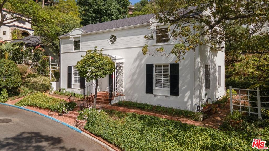 This stately 4-bedroom Colonial sits on a generous 12,208 sq ft corner lot in the highly desirable neighborhood of Lake Hollywood. Drive up Benda Street and you can't miss this beautiful home sitting at the top of the hill. Estimated 113sq feet of street frontage, surrounded by lush landscaping and mature trees, the property offers lovely hillside views from its light-filled rooms. All the wires are underground in the Hollywood knolls - making the tree filled neighborhood even lovelier. The traditional layout features all four bedrooms upstairs each with its own walk-in closet. The spacious living room is anchored by a cozy fireplace, and hardwood floors run throughout the home. The inviting family room boasts a wall of windows overlooking the greenery and opens to a charming brick patio - perfect for lounging or hosting garden parties. There's also a formal dining room with a bay window and a bright, airy kitchen. A detached two-car garage includes a 125 sq ft permitted room - ideal as a home office or additional storage space. The upper portion of the large lot provides extra parking, a place to grow your own vegetables, and can also serve as a play area. Updates include a new roof in 2019, new plumbing in 2023, new furnace in 2023, painted in 2025. In 1965 the home was enlarged, with permits, to include a 4th bedroom, enlarge the den, laundry room and hall. Whether you're drawn to its vintage charm, spacious layout, large lot, or prime location, this home offers the perfect blend of elegance, convenience, and classic Hollywood Hills living - just minutes from world-famous Studios, the Hollywood Bowl, Runyon Canyon, Lake Hollywood, and the nearby communities of Burbank and Studio City. This gem is on the market for the first time in 66 years. Don't miss this rare opportunity to own this warm and inviting home.