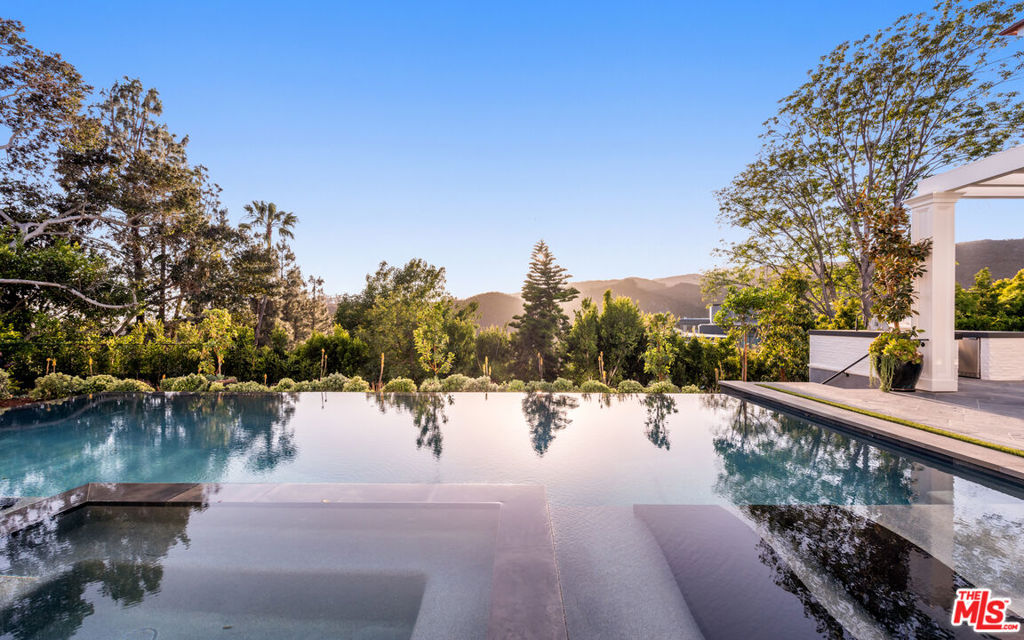 Situated behind privacy gates in the coveted Pacific Palisades Riviera, this newly constructed masterpiece exudes Traditional charm interwoven with a modern sensibility. Envisioned by architect Ken Ungar in collaboration with Story Co., an ultra high end development team made of AMG Capital and Aeries Development, this magnificent home features striking canyon views and is the epitome of luxury. Every inch of the residence exudes extravagance from the lavish finishes to high-end amenities in each room. You will be incredibly stunned as you enter through the welcoming elevated glass front door. The grand detailing is substantial; from the tremendous volume to the remarkable natural light beaming in through the lofty windows and doors from sunrise until sunset. The epicurean kitchen boasts a state-of-the-art Wolf range and three ovens, ideal for hosting large gatherings. The floor plan is purposeful and includes all of today's necessities: a designer office, three-car garage, elevator, two laundry areas, and an impressive lower level with a large recreational room, chic bar, temperature-controlled wine cellar, gym with full bath, over-size media room, and guest quarters. The second level of the home provides an elegant primary suite, with two expansive closets and an oasis-like bathroom that includes a generous spa bath accompanied by a steam shower and endless views. Upstairs also boasts three additional sizable en-suites, walk-in closets, and lounge area. Immerse yourself in the beautifully landscaped backyard featuring a fully equipped outdoor kitchen, infinity-edge pool with Baja shelf and spa, trellis with a built-in fireplace, and an extensive grass area that will keep you in a vacation-like mindset all year round. The residence is concluded with a qualified control smart home system, boasting multiple degrees of perimeter and interior security. Discover the embodiment of craftsmanship and timeless elegance in one of California's most desirable locations.