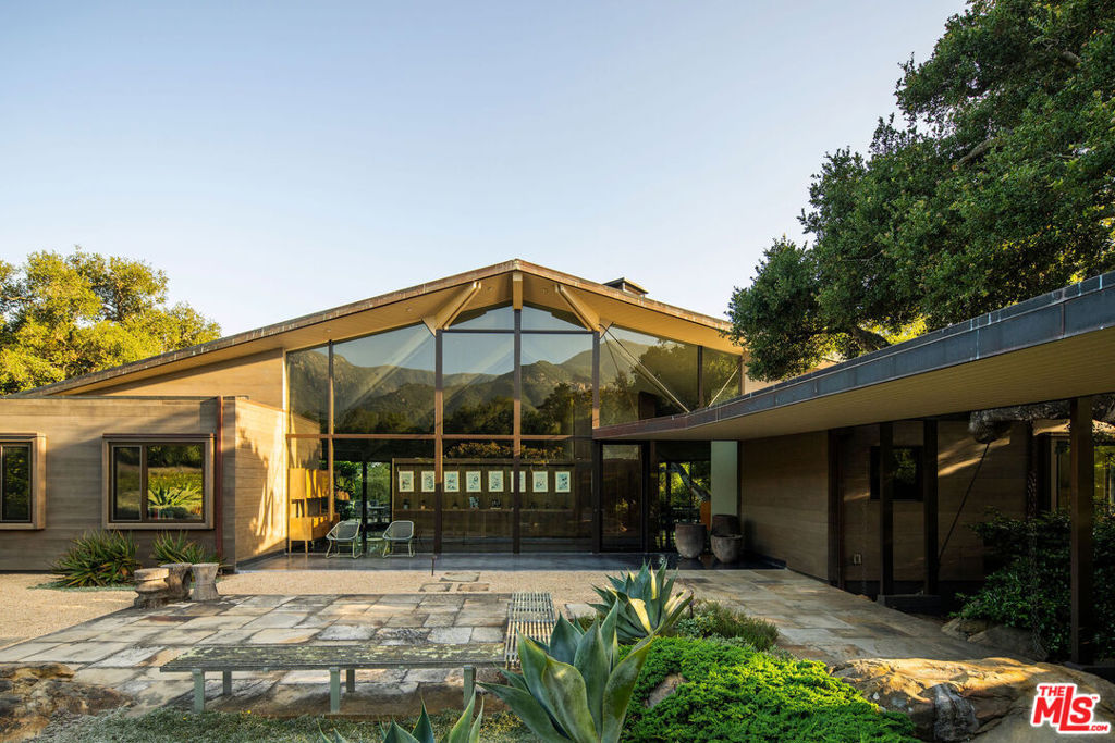 A rare midcentury modern architectural offering in the heart of Montecito, The Erving House, described as a "glass tent" by Time magazine in 1951,is a singular expression of architectural and landscape mastery, gracefully nestled on 2.7 acres of private, artfully curated grounds. Designed in 1950 by renowned architect Lutah Maria Riggs during her iconic modernist phase, and complemented by the legendary California landscape architect Thomas Church, this estate exemplifies the essence of indoor-outdoor living.Enter through private gates, where a meandering driveway weaves beneath a canopy of majestic oaks, setting a serene, cinematic approach to the residence. It culminates in a spacious motor court, where the home's striking flat-roof carport seamlessly marries form and function with timeless elegance.A covered walkway leads to the home's entrance, where a dramatic double-height foyer with floor-to-ceiling glass walls flood the space with natural light and frame expansive views of the surrounding landscape and mountains. This breathtaking entrance sets the tone for a home in constant dialogue with nature.The main living space unfolds with a soaring pitched ceiling, its apex seemingly reaching toward Montecito Peak, and a sculptural, biomorphic Santa Barbara stone fireplace, a subtle homage to Brazilian architect Oscar Niemeyer, Riggs' contemporary and collaborator. Walls of glass, both fixed and sliding, span the length of the room, opening to terraces and gardens and dissolving the boundaries between inside and out.The primary suite is a private retreat, featuring a spa-like bath, dual large dressing rooms, and tranquil views of the gardens and the coastal range. The home office offers inspiring solitude, framed by vistas of mature landscape and mountain ridgelines.The European-style kitchen is outfitted with custom Poggenpohl cabinetry and top-tier appliances, crafted with the serious chef in mind. The adjoining formal dining area also enjoys views of both the northern mountains and the home's terraced gardens and native flora beyond.Adjacent to the main house is a detached studio, providing flexible use, as a guest bedroom, creative workspace, or private retreat, its large windows revealing the natural beauty of mature oaks. Across the property is a serene 1-bedroom, 1-bath creekside guest house offering peaceful accommodations far enough from the main home to feel entirely its own.The grounds, once altered by previous owners,have been thoughtfully revived by landscape architect Susan Van Atta, who honored much of Church's original vision while adding her own artistry through native plantings. Wander through fruit orchards, lavender fields, and raised vegetable gardens, or enjoy a game at the bocce ball court, each element curated for both beauty, sustainability, and enjoyment.The Erving House is more than a residence, it is a living piece of architectural history and one of Montecito's most important homes. It offers unparalleled privacy, serenity, and a lifestyle that celebrates the seamless interplay between nature and design.