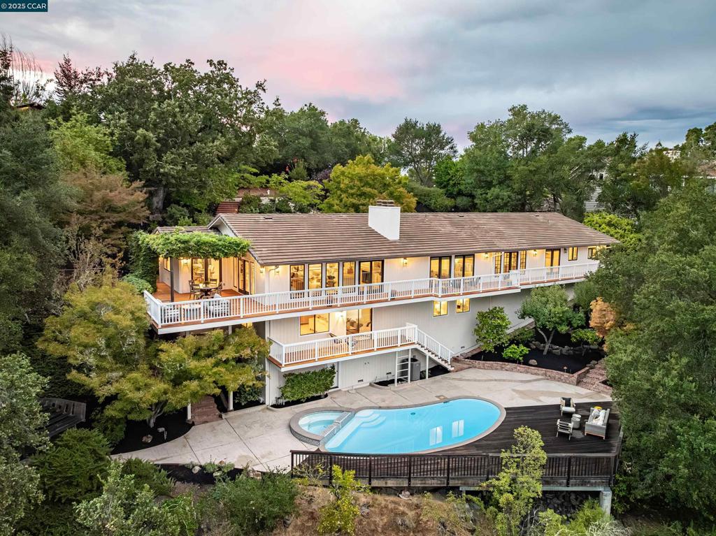 This home sits on a private cul-de-sac amidst nature. A brick stairway meanders down through the immaculate garden to the home’s spacious foyer. It leads to the 300-sq-ft living room, with a paneled ceiling above, parquet hardwoods below, wood-burning fireplace and deck access. Move for dinner to the spacious dining room, with views on 3 sides. The well-appointed kitchen sits alongside, with elite appliances, granite counters, extraordinary garden views through oversized windows, a skylight and oak hardwoods. The principal suite and another large bedroom also are on the main floor, each with an en-suite bath. Both have ample closets; the principal suite has 2. The other bedrooms are downstairs, along with a 450-sq-ft family/rec room (with fireplace). That room leads outside to a deck and down to the swimming pool (resurfaced in 2020), and the adjacent bathroom and outdoor shower. Work or study in the spacious office on the main floor, with deck access and views of surrounding trees. Parking is easy in the 3-car garage and on the cul-de-sac above. For safety, the home’s roof was replaced in 2012 with Eaglelite Ponderosa concrete tiles, and the fully equipped fire station is just down the hill. So, too, are Lafayette’s restaurants and shopping, just minutes away.