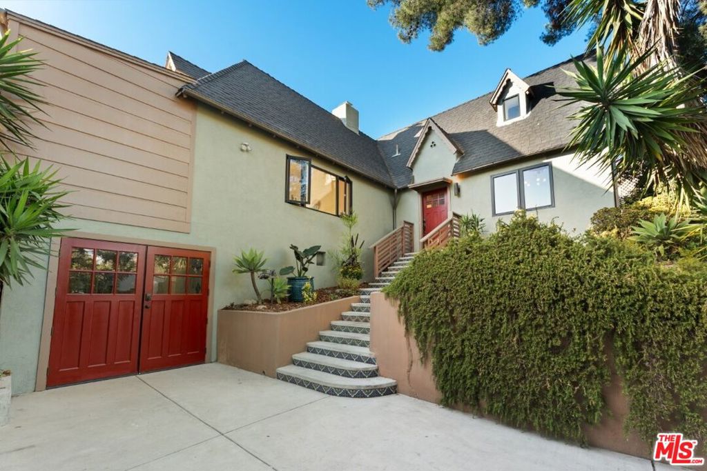 Tucked high in the trees on one of Elysian Heights' most coveted streets, this 1930 tudor has been reimagined for modern living while preserving its original character. The result is a warm, light-filled sanctuary that feels worlds away yet just minutes from Echo Park favorites like Cookbook, Lady Byrd and Bacetti. Vaulted 10-foot ceilings and a decorative fireplace anchor the spacious living room, where French doors open to a sweeping 575 square-foot view deck that spans the length of the home perfect for morning coffee, outdoor dinners, or sunsets over the hills. The remodeled kitchen is both functional and stylish, with quartz countertops, island seating, a wine fridge, and a pass-through window to the patio for effortless entertaining. The primary suite features built-in nightstands and dresser, and an elegant en suite bathroom with walk-in shower. A flexible office or third bedroom provides space for guests or creative work. Additional features include hardwood floors, dual-pane windows, designer lighting, ample storage, and a detached one-car garage that easily doubles as a studio. Below, an expansive lower yard offers room for gardening, play, or future expansion. Elysian Park's trails, the Elysian Heights Elementary Arts Magnet, and neighborhood cafes are just a short stroll away making this rare hillside gem the perfect balance of nature, design, and Los Angeles charm.
