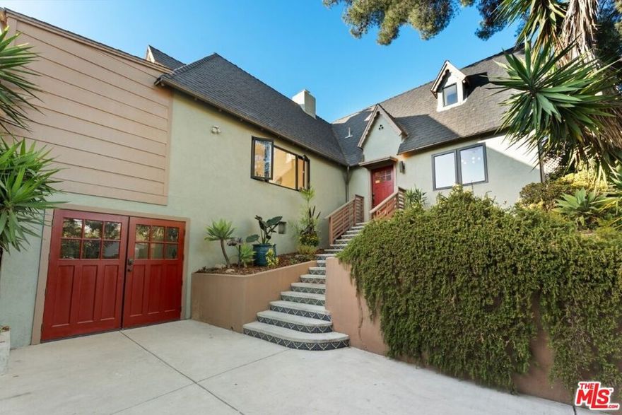 Tucked high in the trees on one of Elysian Heights' most coveted streets, this 1930 tudor has been reimagined for modern living while preserving its original character. The result is a warm, light-filled sanctuary that feels worlds away yet just minutes from Echo Park favorites like Cookbook, Lady Byrd and Bacetti. Vaulted 10-foot ceilings and a decorative fireplace anchor the spacious living room, where French doors open to a sweeping 575 square-foot view deck that spans the length of the home perfect for morning coffee, outdoor dinners, or sunsets over the hills. The remodeled kitchen is both functional and stylish, with quartz countertops, island seating, a wine fridge, and a pass-through window to the patio for effortless entertaining. The primary suite features built-in nightstands and dresser, and an elegant en suite bathroom with walk-in shower. A flexible office or third bedroom provides space for guests or creative work. Additional features include hardwood floors, dual-pane windows, designer lighting, ample storage, and a detached one-car garage that easily doubles as a studio. Below, an expansive lower yard offers room for gardening, play, or future expansion. Elysian Park's trails, the Elysian Heights Elementary Arts Magnet, and neighborhood cafes are just a short stroll away making this rare hillside gem the perfect balance of nature, design, and Los Angeles charm.