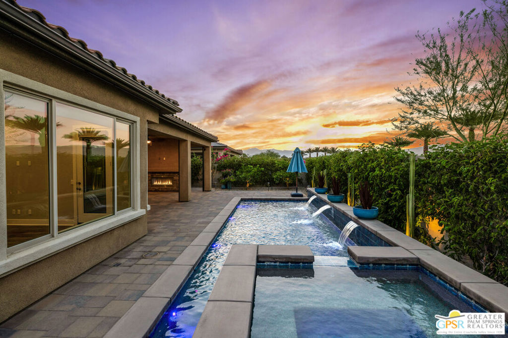 You already know the appeal of Del Webb Rancho Mirage. Now, discover this upgraded Tuscan-style Preserve model, distinguished by over $200,000 in custom upgrades (see list in documents for full details). Desert living is all about enjoying your outdoor space. Teserra designed and built the pool and spa and incorporated three sheer descent waterfalls for a stunning effect. The back patio features a gas fireplace, a misting system, ceiling fans and retractable sunshades. The landscaping is beautifully designed and now has mature plantings that add to this private retreat. The kitchen features upgrades in cabinets, the center island, appliances and lighting. The great room features a gas fireplace, surround sound, custom lighting and an added glass sliding door to the outside. In the primary suite, custom upgrades include a bay window and a French door with direct access to the back yard. The primary bath has a spa-style walk-in shower with solid surface surround, a double vanity and a large walk-in closet. The guest bathroom has a glass enclosed tub/shower. The home features a true third bedroom. The garage has an insulated door with glass panels, additional wall and ceiling insulation, Polyaspartic flooring, and built-in storage cabinets with a workbench. A 15-panel owned solar system keeps energy bills low, while a whole-house water filtration and UV sanitation system ensures pristine water quality. Live intelligently with top-tier smart systems including a Flume water monitor for real-time tracking and leak alerts, irrigation control, Lutron lighting, keyless entry, and iAqualink to manage pool and yard systems remotely.