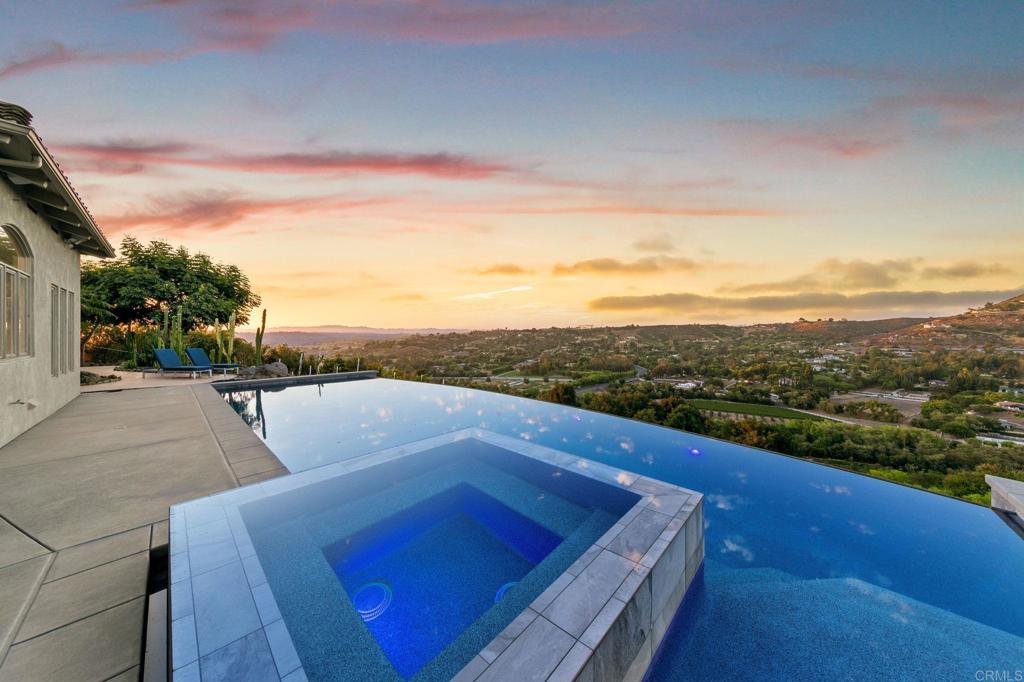 Welcome to Sol Toscano, “Tuscan Sun”—a radiant Mediterranean-inspired retreat gracefully perched atop the rolling hills of Hialeah Rancho Estates. This single-level estate blends timeless elegance with serene seclusion, offering over 4,000 square feet of refined living space on 4.4 acres of exquisitely landscaped grounds. With panoramic vistas of Moody Creek Vineyards and the tranquil valley below, every sunrise and sunset becomes a private work of art. A custom automatic gate, installed in 2023, introduces the property, unfolding into a landscape reimagined by Tomas Ramirez. Over 400 flourishing dragon fruit trees surround the infinity edge pool. Incredible stone paths, secluded seating areas, and a sculptural Stonehenge garden—all softly illuminated by new outdoor sconces that create an enchanting ambiance after dusk. Inside, Sol Toscano is a masterclass in elevated comfort and craftsmanship. The home was fully repainted in 2023, creating a clean and refined backdrop for warm finishes, custom millwork, and designer lighting. Expansive Fleetwood doors and windows frame sweeping views and effortlessly blend the interior with the outdoors—featured in the living room, front entry, and the primary suite’s trifold door. At the heart of the home, the chef’s kitchen was completely remodeled in 2025. It features bold black velvet granite countertops, a central island for gathering, and an all-new suite of high-end Café appliances, offering both performance and sophistication. The private east wing hosts a tranquil primary suite, featuring a spa-style bathroom fully renovated in 2023. Dual rain showers, a deep soaking tub, and a stunning Starlix glass enclosure evoke a luxurious, spa-like experience at home. A custom walk-in closet adds both practicality and elegance. The west wing offers two beautifully remodeled guest en-suites, one of which includes a new pedestal sink. This wing also features a bonus room, a laundry area, and a custom home office with built-in cabinetry and its own secret garden nook—ideal for quiet work or creative retreat. The true centerpiece of Sol Toscano is its resort-style outdoor haven: a 40-foot saltwater infinity pool and spa that flow effortlessly into the valley below. With a modern self-regulating system, upgraded heating, and a Pebble Sheen surface, this poolside escape is both low-maintenance and indulgent. Additional features include a new dual-zone HVAC system, whole-house generator, upgraded water heater, restored fireplaces, a three-car garage with newly finished epoxy flooring, EV charging capability, integrated indoor and outdoor sound systems, and statement lighting throughout. Sol Toscano is more than a home—it is a curated lifestyle of grace, serenity, and refined living in one of Bonsall’s most breathtaking settings.