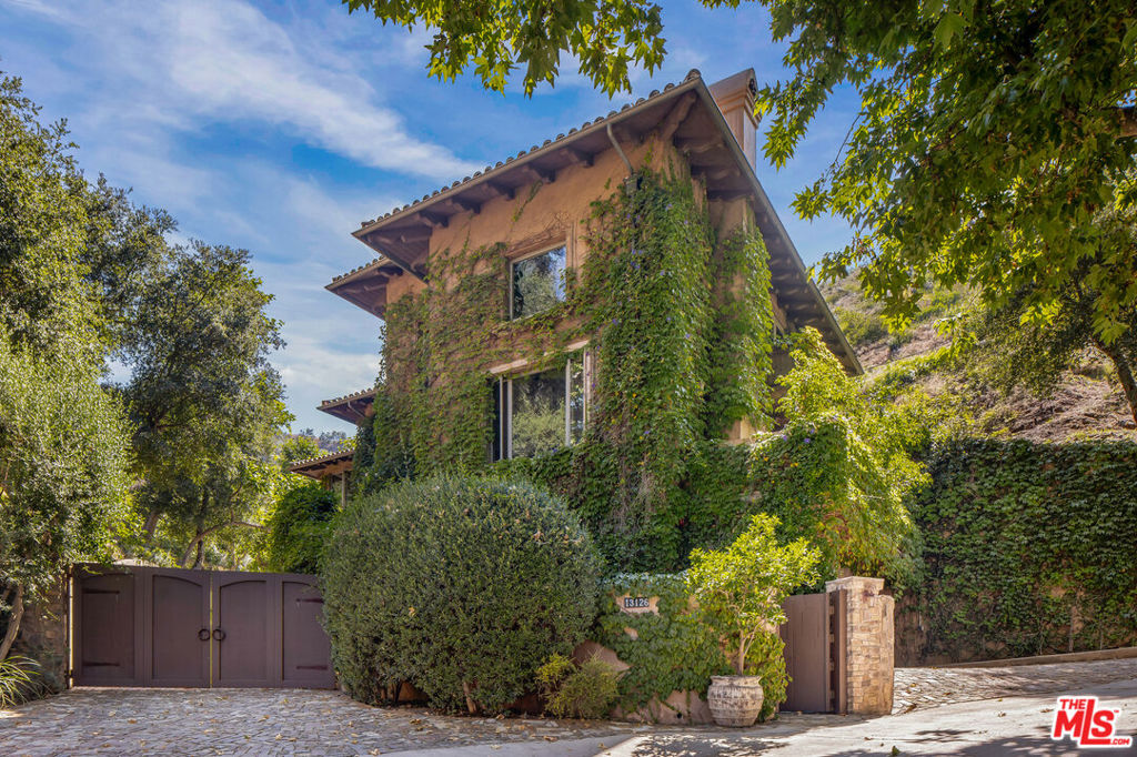 Nestled on an expansive, storybook parcel in the heart of Mandeville Canyon, this extraordinary estate feels worlds away from Los Angeles, yet remains just moments from the best of the Westside. Surrounded by lush landscaping, a sprawling meadow framed by a ranch-style fence and enchanting gardens, the property offers a rare blend of natural beauty, privacy, and old-world charm. The grounds are truly magical, with sun-drenched patios, peaceful verandas, and a lagoon-style pool featuring a grand waterfall, creating a resort-like atmosphere. Tucked behind gates, the home evokes the romance of the Tuscan countryside, blending timeless materials with European elegance. From the forged ironwork to custom stone and wood finishes, artisan workmanship is evident throughout. Venetian plaster walls add warmth and refinement throughout the interiors, while a striking oversized front door - over a century old with detailed engraving - sets a dramatic tone upon entry. Inside, the grand formal living room is a true showpiece, with ceilings soaring over 20 feet, dramatic wood beams, and elegant built-ins. French doors open to a spacious balcony, flooding the space with light and connecting the interiors to the surrounding beauty. A gourmet kitchen flows seamlessly into a cozy breakfast nook and inviting family room, both of which open to the outdoor living areas. The covered patio is ideal for entertaining, featuring a wood-burning clay pizza oven and a built-in stainless-steel grill. The pool, spa, and sweeping meadow accommodate both relaxation and large gatherings. Upstairs, the luxurious primary suite offers a private retreat with a fireplace, spa-like bath, walk-in closet, and a secluded balcony overlooking the verdant grounds. Two additional ensuite bedrooms provide comfort for family and guests, while the lower level offers a flexible fourth bedroom or gym and a wine cellar with custom stone and wood finishes.Warm, authentic, and entirely unique, this is more than a home - it's a private escape that captures the romance of the European countryside, nestled in the heart of Brentwood.