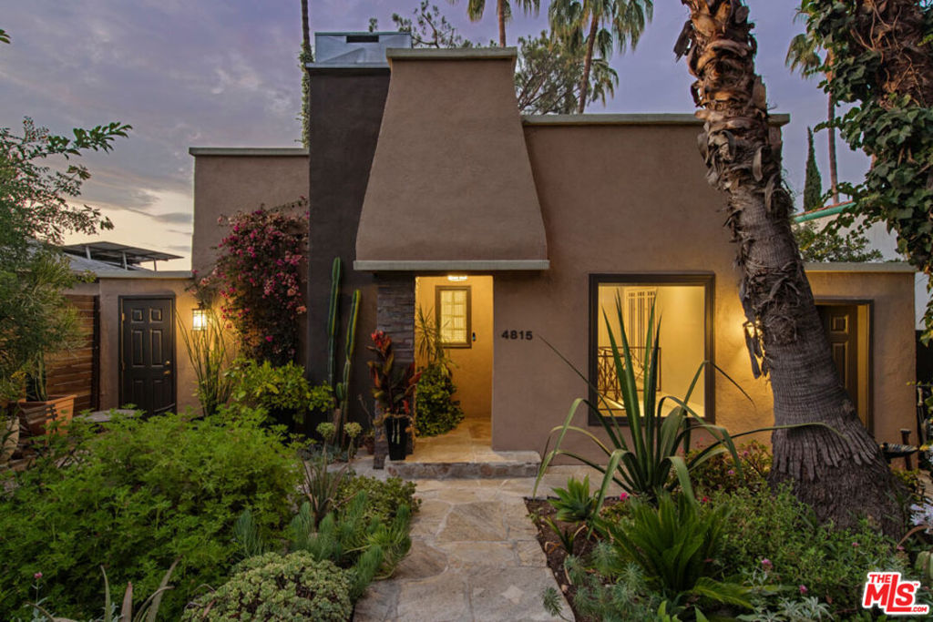 Perched on a private cul-de-sac in Highland Park, this 1924 hillside home is a quiet, luminous retreat wrapped in lush California flora. The two-level layout is open and easy, with a skylit living room featuring elegant cornice moldings, a classic fireplace, and sweeping hillside and mountain vistas. The kitchen has stone counters and ample storage, with access to a breezy balcony for morning coffee. Two bedrooms include one with French doors opening to a pergola-covered deck; downstairs, a second bedroom with ensuite bath and private entry is ideal for guests or workspace. All around: greenery, birdsong, and breathtaking views. The terraced backyard is an entertainer's dream, a verdant escape with fruit trees, shaded lounging areas and a jacuzzi. A large Tuff Shed with AC and power adds space for creative use; amenities include central heat/air and laundry. Just two blocks from York and close to Figueroa and local favorites Wildcrust, Belle's, Joy, Kumquat Coffee, Goldburger, and more.