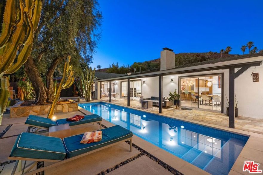 Located in Lakeridge Estates, a mid-century neighborhood near the Lake Hollywood Reservoir, 6570 Lakeridge Road is a 2,201 square foot ranch-style home that has been thoughtfully redone for modern living. Sunlight moves easily through an open floor plan that leads to multiple outdoor areas designed for entertaining. A new pool is ready for the summer heat and evenings spent under the stars. The large living and formal dining rooms share a two-sided fireplace, one functional and one decorative, and connect to a reimagined kitchen with a quartz-wrapped island, Viking double ovens, custom ventilation hood, and fixtures that recall the home's original design era. The primary bedroom opens directly to the pool deck. Its en-suite bathroom includes a soaking tub, step-in shower, dual sinks, and recently installed chrome fixtures. Two additional bedrooms share a second bathroom, with one room offering direct access. An oversized two-car garage with direct entry includes built-in storage and a raised laundry platform with side-by-side LG washer and dryer, installed two years ago. A gated perimeter with driveway and pedestrian gates adds privacy and extra off-street parking. A five-camera security system and 24-hour live neighborhood patrol offer additional peace of mind. Set on a 12,027 square foot lot, the property is located near hiking trails, the Hollywood Bowl, studios, and markets including Whole Foods and Trader Joe's. This is Southern California living with clarity and intention.