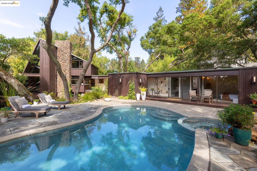 Discover a rare architectural gem in Berkeley’s coveted Uplands neighborhood. Designed by architect Lyman Jee for his family, this sun-filled home is a private retreat that seamlessly blends design, nature, and tranquility. Set on a serene, oak-studded parcel, the home is introduced by a distinctive copper roof and a stained-wood footbridge spanning a rippling creek—a magical entry that sets the stage for what’s inside. Soaring ceilings, walls of glass, and a dramatic floor-to-ceiling stone fireplace create an inviting interior that frames the lush, landscaped surroundings. With three bedrooms, three full baths, & exceptional indoor-outdoor flow, this home was designed for both relaxation & entertaining. Step outside to the pool & hot tub for resort-style living, or enjoy the peaceful connection to nature from every room. The location offers the best of Berkeley living: Close to Claremont Resort, Fournee, Peets, the Elmwood’s charming shops and cafés, transbay transit, and it’s just minutes from UC Berkeley. A stunning piece of architecture, this home is ready for its next discerning owner who values design, tranquility, and a truly unique setting.