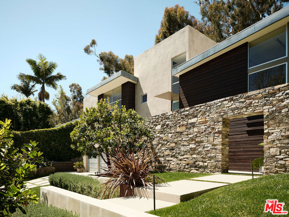 Nestled in the sought-after enclave of Rustic Canyon, this architectural gem was artfully crafted by acclaimed architect Michael Kovac. The home embodies completely custom, timeless design ensuring quality in every corner. Step inside to discover a formal yet relaxed living room effortlessly flowing to an additional open-concept living and dining space. Artistically framed floor-to-ceiling windows flood the rooms with natural light complimenting the warmth and richness of the hardwood accents while allowing the polished cement floors, and Boffi kitchen with Gaggenau appliances, to add a touch of modern sophistication. Ascend the exquisitely designed staircase to reveal a luxurious primary suite welcoming a sitting room, steam shower, office loft and private terrace. Envisioned for relaxation and entertaining, your outdoor oasis awaits featuring a marvelous infinity pool + spa, waterfall and picturesque treetop views. Four additional bedrooms, six bathrooms and a vast three-car garage complete the home. Don't miss this opportunity to call this Rustic Canyon gem home! * Home is 5,566 SF on public records