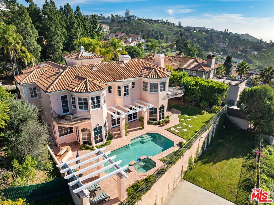 This elegant Mediterranean-style residence blends timeless architecture with refined modern living, ideally located in the Pacific Palisades Highlands amid mature palms and manicured landscaping. The impressive entry opens to a dramatic interior highlighted by a sweeping, curved grand staircase that serves as a striking architectural centerpiece, immediately setting the tone for the home's scale and craftsmanship. Sun-filled living spaces feature soaring ceilings, hardwood flooring, and arched windows and doors that create a seamless connection between indoor and outdoor areas. The thoughtfully designed floor plan offers multiple gathering spaces for both formal entertaining and everyday living, enhanced by custom details and elegant architectural transitions throughout. The primary suite is a private retreat, featuring a balcony with ocean views and refreshing coastal breezes, an ideal setting to unwind at the start or end of the day. Additional bedrooms and living areas provide flexibility and comfort across multiple levels. A dedicated music studio adds valuable flexibility to the home, offering versatile use as a creative space, media room, office, or additional flex room to suit a variety of lifestyle needs. Outdoors, the backyard offers a resort-style setting with a pool and spa, expansive patio areas, and lush landscaping designed for relaxation and entertaining. Elevated positioning enhances privacy while showcasing scenic hillside surroundings. Located in the Pacific Palisades Highlands, this exceptional property combines grand architectural elements, inviting indoor-outdoor living, and a highly desirable setting. Sq footage includes approximately 600 sq ft of enclosed garage space, which has been converted into a studio/ flex space.