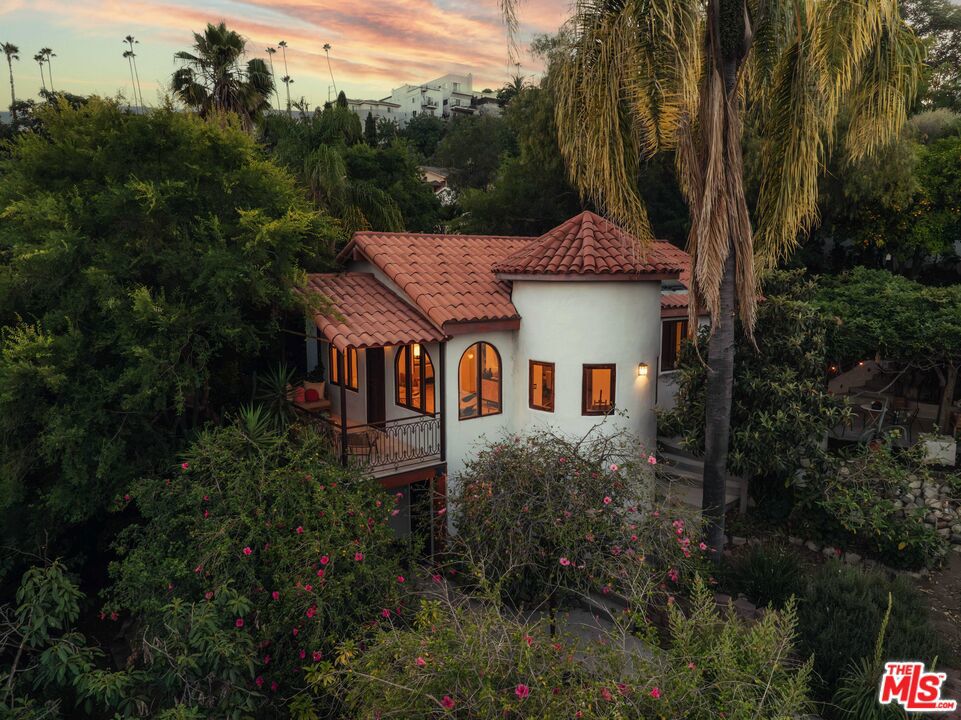 Welcome to your own private sanctuary in the hills of Los Angeles. Hidden behind gates and surrounded by nature, this one-of-a-kind Spanish compound is a place of beauty, peace, and quiet magic. Wander the gardens, meditate, breathe -- this is a home that lets you tune out the noise and reconnect with what matters. Enjoy yoga under a canopy of fragrant wisteria, share a meal beneath the trees, and watch the light shift across the mountains. Set across 5 lots totaling more than 20,000 square feet of terraced gardens, with incredible views from every angle, the property is filled with fruit trees, flowering vines, and raised bed gardens large enough to grow everything you need for a true farm-to-table lifestyle. Stone paths connect a series of outdoor rooms carved into the hillside, each with its own mood and view. Nestled within the lush landscape, the main house is a classic example of Spanish architecture, where soaring ceilings, wood beams, and arched windows create a warm and timeless atmosphere. The living room opens to a covered balcony with hillside views, while a peaceful courtyard wraps around the dining room and primary bedroom. From nearly every window, you'll see beautiful greenery: treetops, distant mountains, and layered gardens that invite a slower pace. With beautiful arched doors leading to the private courtyard and gardens, this home embodies the indoor-outdoor flow that makes California living so special. Downstairs features a completely separate 1 bedroom suite, perfect for family, guests or a second office. The detached casita sits deeper in the garden and includes bedroom, flex/office, bath, and private deck. It's ideal for guests, creative work, or quiet retreat. Minutes from DTLA but a million miles away, this truly special home is a rare opportunity to live in a space that feels both cultivated and completely wild.