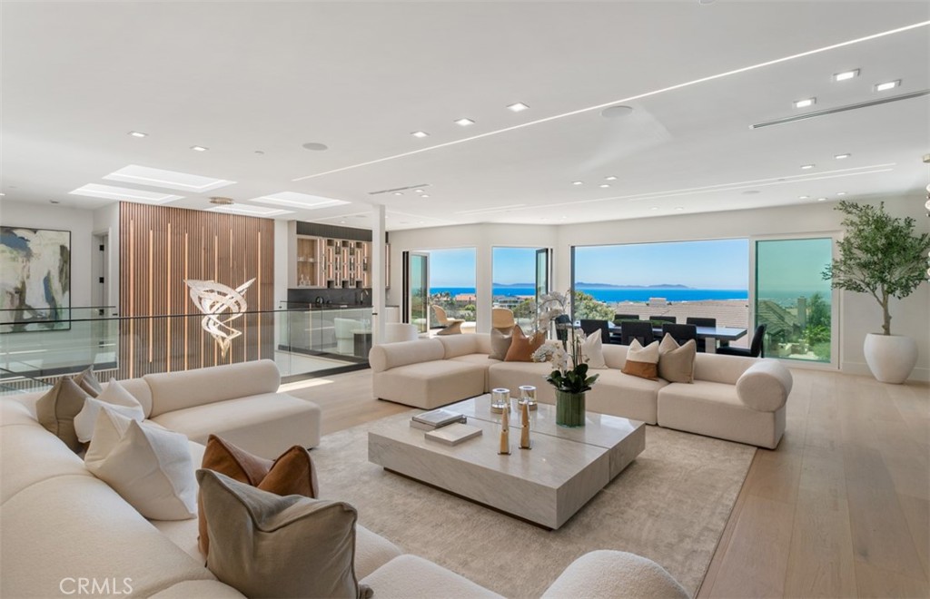 Perched at the end of a quiet cul-de-sac within the exclusive guard-gated enclave of Harbor Ridge, 4 Narbonne is a stunning showcase of design, function, and luxury. Completely reimagined, this architectural gem blends striking modern aesthetics with a warm, inviting ambiance—perfectly tailored for entertaining and everyday living. Beyond a private entry gate and custom oversized front door, you’re welcomed into a dramatic open-concept layout filled with natural light, curated finishes, and an effortless indoor-outdoor flow. The main level offers three spacious bedrooms, including a junior primary suite with ocean views, and two secondary bedrooms that overlook a serene water feature. A sleek lounge with a fireplace, bar, and media wall adds to the home’s entertainer appeal. Take the elevator upstairs, where panoramic views span the Pacific Ocean, Catalina Island, Newport Harbor, and city lights that stretch to downtown LA. Designed for both grandeur and comfort, this level features two additional bedrooms—one currently used as a home office with its own balcony—as well as a show-stopping primary suite wrapped in floor-to-ceiling glass. The spa-like bathroom and boutique-style closet complete the experience. The heart of the home includes both a front-facing designer kitchen and a full secondary prep kitchen, flanked by a breakfast nook, formal dining area, double fireplaces, and walls of sliding and bi-folding doors that dissolve the line between indoors and out. Step into your own private resort: a spectacular outdoor oasis with a pool, spa, dry sauna, multiple waterfalls, a built-in BBQ island, fire table, and ample lounge and dining areas—designed to impress and built to entertain. With every box checked—guard-gated security, panoramic views, stunning finishes, and true turnkey luxury—this is coastal living at its finest.