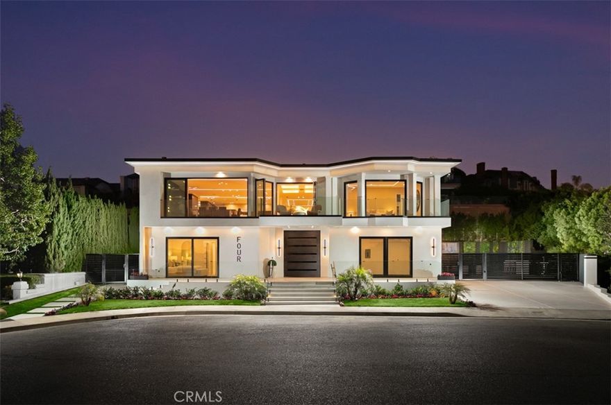 Perched at the end of a quiet cul-de-sac within the exclusive guard-gated enclave of Harbor Ridge, 4 Narbonne is a stunning showcase of design, function, and luxury. Completely reimagined, this architectural gem blends striking modern aesthetics with a warm, inviting ambiance—perfectly tailored for entertaining and everyday living. Beyond a private entry gate and custom oversized front door, you’re welcomed into a dramatic open-concept layout filled with natural light, curated finishes, and an effortless indoor-outdoor flow. The main level offers three spacious bedrooms, including a junior primary suite with ocean views, and two secondary bedrooms that overlook a serene water feature. A sleek lounge with a fireplace, bar, and media wall adds to the home’s entertainer appeal. Take the elevator upstairs, where panoramic views span the Pacific Ocean, Catalina Island, Newport Harbor, and city lights that stretch to downtown LA. Designed for both grandeur and comfort, this level features two additional bedrooms—one currently used as a home office with its own balcony—as well as a show-stopping primary suite wrapped in floor-to-ceiling glass. The spa-like bathroom and boutique-style closet complete the experience. The heart of the home includes both a front-facing designer kitchen and a full secondary prep kitchen, flanked by a breakfast nook, formal dining area, double fireplaces, and walls of sliding and bi-folding doors that dissolve the line between indoors and out. Step into your own private resort: a spectacular outdoor oasis with a pool, spa, dry sauna, multiple waterfalls, a BBQ island, fire table, and ample lounge and dining areas—designed to impress and built to entertain. With every box checked—guard-gated security, panoramic views, stunning finishes, and true turnkey luxury—this is coastal living at its finest.