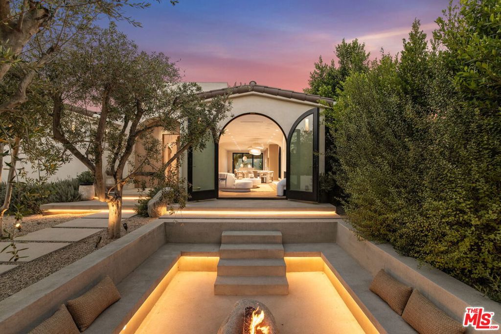 Conveniently located just minutes from the highly sought-after Larchmont Village, this manicured estate transports you to a world of design and distinction. Mature olive trees and lush surroundings set the stage for something special, where a custom-designed sunken fire pit makes a striking architectural statement. Artistic in form and function, it merges sculptural presence with a warm, welcoming ambiance. The residence embodies a refined desert modern aesthetic with organic textures, contemporary curves, Fleetwood sliding doors, Roman clay walls and travertine stone adding timeless elegance throughout. A chef's kitchen anchors the living spaces with precision and style, outfitted with Miele appliances, custom cabinetry and an expansive island. Herringbone-laid hardwood floors add an artisanal touch that carries throughout. The backyard is a private oasis, enveloped by mature hedges that provide both seclusion and tranquility. Thoughtfully layered landscaping and lush greenery create a serene backdrop for relaxation or entertaining. Every element has been curated to embody a sense of artistry, lifestyle and unparalleled vision. Beyond the gates, you're moments from acclaimed restaurants, trendy shops, the prestigious Hancock Park Country Club and a welcoming, family-friendly community.