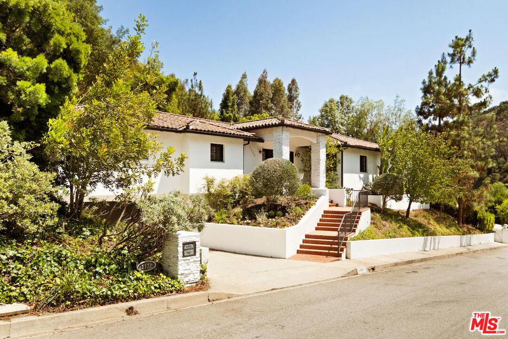 Nestled in a lush canyon in lower Bel Air, and one of the most charming homes on the street, 1132 Chantilly Rd is a single-level, turnkey home featuring three bedrooms and three bathrooms. Set above the street with striking black double front doors, wrought iron lanterns, a brick stairway leads to a covered entry framed in white stone. A wood-burning fireplace anchors the living room, which connects to a dining area that opens to the outdoor terrace through French doors. The kitchen includes Wolf appliances, stone countertops, generous storage, a breakfast nook, and a window-lined area ideally suited for a coffee corner. The primary suite includes its own fireplace, walk-in closet, seating area, and direct access to a private backyard. The en-suite bath features limestone finishes, dual vanities, a soaking tub, and a steam shower with dual heads. Two additional en-suite bedrooms are positioned to bring in natural light through well-placed windows. Surrounded by mature greenery, the outdoor areas offer multiple spaces for lounging and alfresco dining. A compelling offering in lower Bel Air, where location, size, and quality rarely align at this price point.