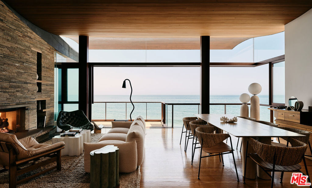 This architectural marvel features an intricate blend of vertical and horizontal planes of wood, stone, and metal, bathed in natural light streaming through sliding glass walls, strategically placed skylights, and an artistic glass floor. Designed by architect Jay Vanos, the finest woodworkers used American Southern cypress for its durability and golden hue on the floors and walls, complemented by a soaring wave redwood ceiling. With ocean views from almost every room, the home boasts a great room with a fireplace, a sitting/dining area, a gourmet kitchen with high-end appliances, and glass walls that open to an outdoor deck perfect for intimate or lavish entertaining. It includes three spacious master suites with fireplaces, luxurious spa-like baths, large closets, and ocean view decks, along with two additional bedrooms. Additional spaces include a sun-filled office/den, a cozy reading/library area, an art studio, an indoor sauna, a zen-style wellness area with sauna and cold plunge, and more. Steps lead to a lower-level surfboard storage area and provide direct access to the beach and renowned Latigo surf spot, making it an ideal home for surfing enthusiasts.