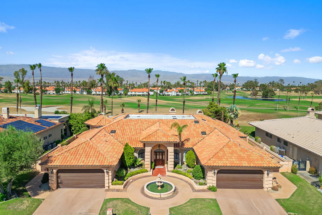 Welcome to a one-of-a-kind estate nestled in the prestigious Desert Falls Estates in Palm Desert. This custom-built home is strategically positioned on the golf course and features breathtaking panoramic mountain views. Built in 1991, this meticulously maintained residence boasts 4 spacious bedrooms, 5 luxurious bathrooms, and 5,003 square feet of architectural charm and luxury. From the grand fountain courtyard entryway to the vibrant interior spaces, every detail has been meticulously crafted with vaulted and coffered ceilings, rich architectural details, and custom-built-ins. The home features multiple living areas, each with its own fireplace, and the custom wet bar is perfect for entertaining or relaxing in style. The gourmet kitchen boasts a large island, a gas cooktop, ample cabinetry, and a sunny breakfast nook that opens to the backyard patio. The spacious primary suite is a private retreat complete with a cozy fireplace, golf course views, a spacious walk-in closet, and a spa-like bathroom featuring dual vanities, a jetted soaking tub, an oversized walk-in shower, and a cedar-lined sauna. Each guest bedroom is generously sized and well-appointed, providing comfort and privacy for family or visitors. Step outside to your private backyard oasis, where an infinity-edge pool and spa overlook the lush fairway with a striking panoramic mountain views. The large covered patio offers multiple areas for lounging, dining, and entertaining. A four-car garage is perfect for car collectors, golf cart storage, or accommodating guests with ease. Located behind the gates of Desert Falls Country Club, residents enjoy access to golf, tennis, pickleball, and a full-service clubhouse. Whether you're hosting a lively celebration or enjoying a peaceful morning with coffee and panoramic views, this home offers an unmatched lifestyle in one of Palm Desert's most desirable golf course communities.