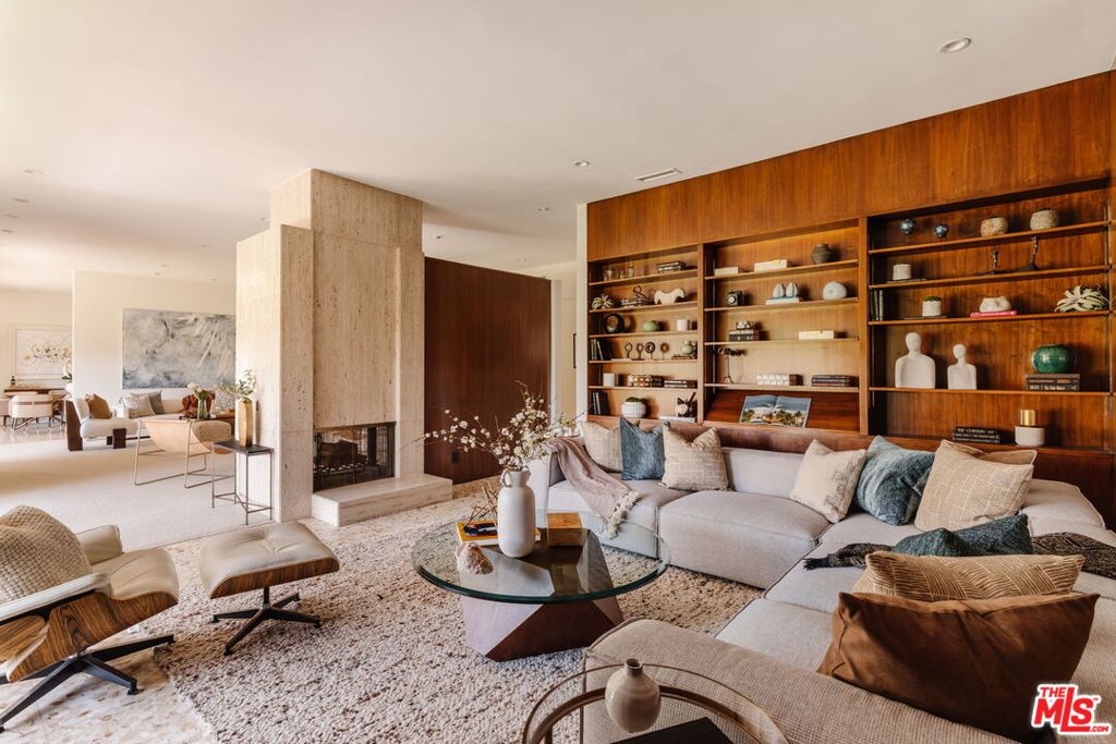 Designed in 1966 by acclaimed architect William Krisel, this Brentwood residence stands as a preserved study in California modernism, where light, landscape, and architecture converge with rare precision. Celebrated for shaping the postwar aesthetic of Southern California, Krisel's vision was defined by clean lines, open living, and a belief that design should elevate everyday life -- and this home embodies that philosophy at every turn. Set discreetly above the street, the single-level floorplan reveals its architectural intent upon entering from the original double doors and Italian terrazzo floors to expansive, unobstructed views from the communal living spaces. A two-sided travertine fireplace anchors the interiors, separating the formal entertaining room from a more intimate lounge framed by warm wood built-ins and a chic wet bar. Walls of glass slide open to a covered patio that spans the length of the home, where serene canyon and mountain views unfold across a grassy backyard shaded by mature trees and layered landscaping. The property extends down the hillside, creating both privacy and the opportunity to design a true resort-style retreat. The reimagined kitchen retains its modernist spirit with a sculptural island, skylight, ample pantry storage, and sleek contemporary finishes. A breakfast nook and built-in workstation enhance daily living, while the adjacent formal dining room and entertaining areas flow seamlessly to the outdoors. Four bedrooms include a tranquil primary suite with generous closet space and a luxurious stone-clad bath. Additional amenities include brand new AC/Heater units, laundry room, and a two-car attached garage. Ideally situated in Kenter Canyon, the home feels worlds away yet remains close to Westside favorites like the area's fine dining, boutiques, top rated schools, and is just minutes to the beach. Preserved with integrity, this rare Brentwood offering honors the legacy of one of California's most celebrated architects and presents an opportunity to inhabit an authentic work of modernist design.