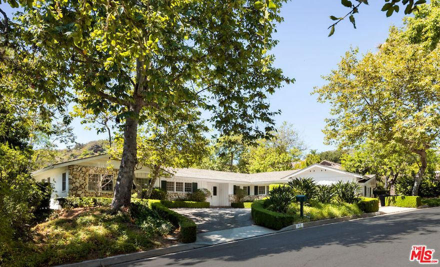 Privately tucked away in the prestigious Trousdale Estates, this charming 4,000 SqFt ranch-style home seamlessly blends traditional comfort with modern luxury. This timeless 4 bed, 6 bath residence exudes classic Beverly Hills allure while offering a unique opportunity for potential updates or expansion. Guests are welcomed into the formal living room by an impressive stone clad fireplace, hardwood floors, and wood-beamed ceilings which are carried throughout. Cozy den features impressive built-in bookshelves and is enhanced by a mirrored wet-bar, ideal for entertaining. An indoor brick barbecue is a notable focal point of the formal dining in addition to the exquisite French doors that thoughtfully lead to the expansive brick-paved patio to enjoy meals al-fresco. Drenched by natural sunlight, the renovated kitchen boasts high-end appliances, including dual ovens, and an abundance of counter space with access to the fenced in turf dog run. An expansive primary suite with luxurious en-suite, and generous walk-in closet is intentionally placed at the wing of the house. This highly functional floorpan is complete with 3 additional bedrooms and a wood paneled office. Spanning 21,000+ SqFt and framed by a canopy of lush greenery, this lot is a tranquil haven. A massive in-ground pool and expansive grassy pad are surrounded by mature landscaping and capture breathtaking, panoramic canyon views. A gazebo placed at the end of the yard is the perfect for soaking up the California sun while admiring the serene backdrop. With a circular driveway and attached two car garage, parking is ample and convenient. An extraordinary opportunity to reside in one of the most highly coveted enclaves.