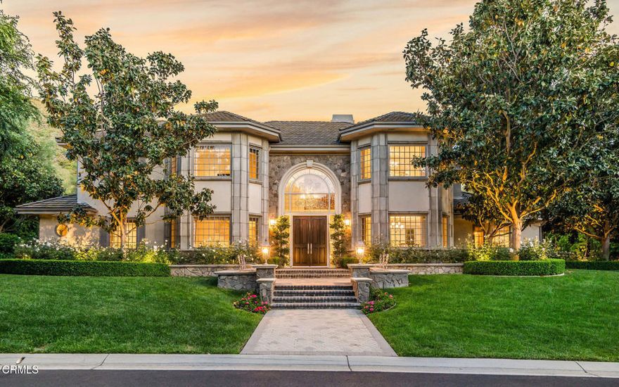 Nestled on a quiet cul-de-sac, in Guard Gated North Ranch Country Club Estates, this French Provincial-style estate is a masterclass in refined living and timeless elegance on a sprawling over 1 acre lot. A grand mahogany front door, capped by a beveled glass window, and framed by lush rose bushes, hedges and magnolia trees introduce you to the luxury and serenity within. The main level features chiseled-edge Versailles-pattern travertine floors throughout the sophisticated spaces. A step-down media room, with blackout drapes and an onyx-topped wet bar is perfect for movie nights. A library offers a quiet retreat, while a spacious office with built-in desks provides flexibility--easily converted into a bedroom suite. An additional main-level bedroom includes an accessible, age-in-place bathroom, ideal for multigenerational living. The heart of the home is the impressive cook's kitchen. Finished with onyx countertops, huge island, carved limestone sink and hammered-nickel prep sink, the space is equipped with high-end appliances, including four ovens, and a custom limestone/pewter hood - all tailored for serious cooks. Custom cabinetry includes a pop-up mixer cabinet and top lighting. A butler's pantry and over-sized breakfast nook, complete the space. A dining room with a glowing ceiling and a spacious family room with coffered ceilings and a marble fireplace are perfect settings for memorable meals, parties and relaxation. A 350-bottle capacity wine room is a collector's dream! The primary suite is a dream with its carved wood and marble fireplace, sitting area and dual walk-in closets. The en-suite bath features a freestanding tub, large glass and marble shower with Waterworks waterjet designed wall, and built-in vanity--with views of the beautiful grounds. Two additional guest suites with well-appointed ensuite baths round out the upstairs. The backyard is a showstopper. Nearly 1,000 blooming rose bushes create a dramatic backdrop against the hillside of this paradise. A Pebbletec salt water pool and spa sit in the center of an oasis that includes an elevated fireplace pavilion, built-in artisan BBQ area and multiple seating areas. The entire space is surrounded by vibrant landscaping, creating an elegant outdoor retreat. From the moment you arrive, the home makes a statement - elegant, warm, and impeccably maintained. In the heart of one of Westlake Village's most idyllic neighborhoods, this home is built for real life living in luxury and convenience.