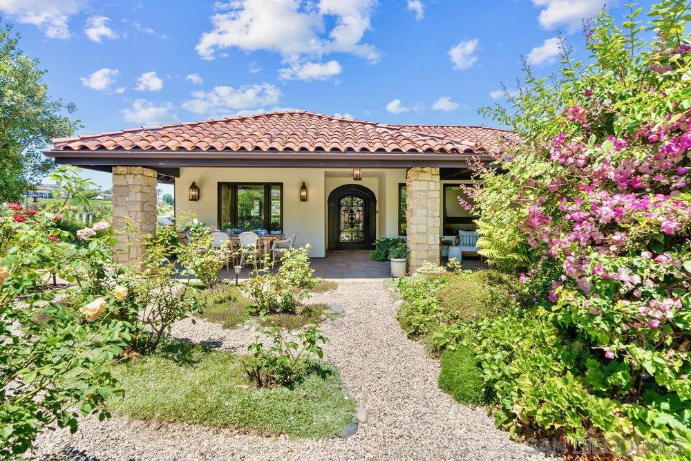 Villa Blanca isn’t just a home—it’s a Solana Beach state of mind. While the Zillow junkies are still swiping through endless listings in search of “coastal charm,” you’ve already found the real deal. A rare, single-level stunner perched on over half an acre above the Lomas Santa Fe Country Club—no HOA overlords, no Mello Roos, no nonsense. Just panoramic views in every direction: gardens, trees, greens, and meadows. It’s so idyllic you’ll start canceling plans just to stay home—because honestly, a glass of wine at sunset by the fire pit never sounded so good. Tucked behind a private gate at the end of a peaceful cul-de-sac, the home unfolds like it was built for ease—wide-plank hardwood floors underfoot, antique and custom iron and wood doors that feel like they’ve got stories, high-end everything, and finishes chosen by someone who actually understands timeless design. The entire space flows effortlessly indoors and out, the way only Solana Beach’s near-perfect weather allows. The kitchen? It’s not a kitchen. It’s a command center for your best life—Wolf and Thermador appliances, artisan cabinetry, granite counters, and room for everything from slow Sunday breakfasts to dinner parties that drift out to the veranda. You’ll pretend people gather elsewhere, but they always end up here. The grounds are a masterclass in Southern California living—fully landscaped, fenced and irrigated, with 20+ fruit trees, organic raised beds, fountains, heirloom roses, a pollinator meadow, and yes, even a designer chicken coop. You read that right. Chickens—with better housing than most people. The primary suite is a sanctuary of soft light and garden views, complete with a spa bath that feels like a boutique hotel got lost in Provence. And just when you think you’ve seen it all, a detached studio floats above the 3rd green with pond views—perfect as an office, art studio, or yoga retreat. The entire lot is elevated, private, and wrapped in mature greenery—because real luxury is not being seen unless you want to be.