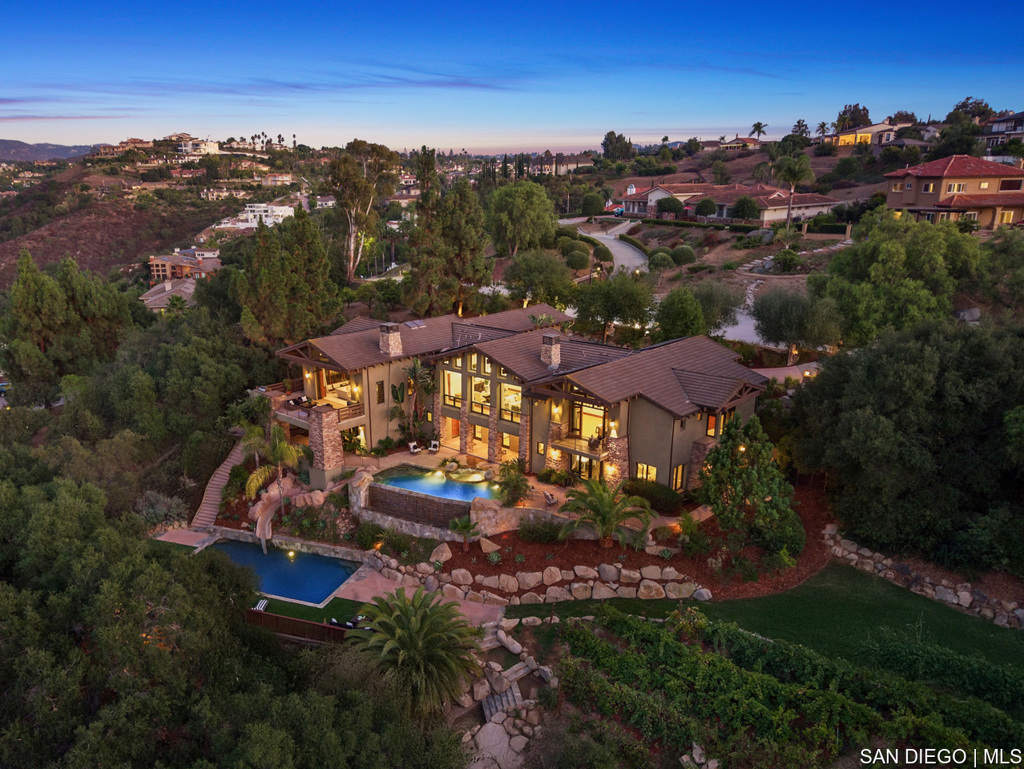 Nestled in the hills of San Diego, 18787 Aceituno St is a Craftsman-inspired masterpiece modeled after the iconic Torrey Pines Lodge, offering panoramic views and resort-style living. This 5-bedroom home with office and bonus room features soaring vaulted beam ceilings, expansive living spaces, and vanishing pocket doors for seamless indoor-outdoor flow. The gourmet kitchen boasts dual Miele dishwashers, a Viking professional suite, built-in BBQ, and Sub-Zero refrigeration, ideal for entertaining. The entry-level master retreat includes a fireplace, private balcony, spa-like bath, and dual walk-in closets. Outdoor living is highlighted by a vanishing-edge pool with waterslide, multiple terraces, sweeping views, and a boutique vineyard. The family level offers a game room, wet bar, and en-suite bedrooms opening to the backyard. Modern upgrades, whole-home audio, WiFi pool controls, multi-zone HVAC, fire-aware sprinklers, and fully owned solar, ensure efficiency and comfort. A 3-car garage and fine craftsmanship complete this ultimate Southern California lifestyle.