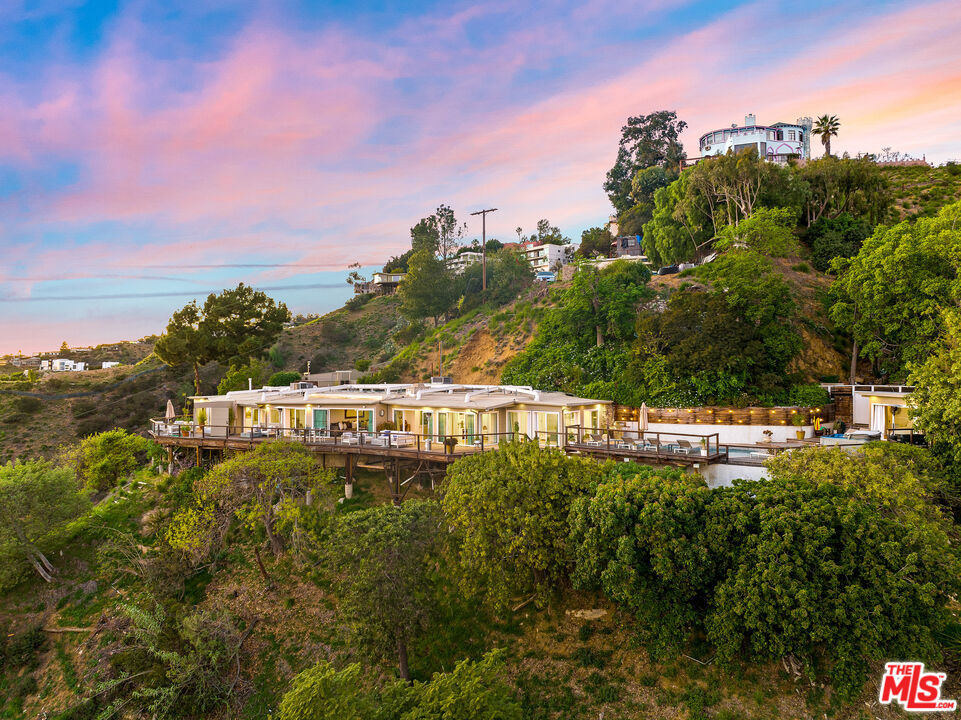 ONE OF A KIND, TROPHY ESTATE! Tucked above Sunset Plaza in the Hollywood Hills, this one-of-a-kind contemporary retreat offers six bedrooms, six bathrooms, a pool, and some of the most breathtaking views in Los Angeles, stretching from downtown to the ocean. Set on 1.37 acres with no rental restrictions, the property is uniquely positioned for both personal use and investment potential.The main residence features four bedrooms, four bathrooms, living and dining areas, kitchen, laundry, and a flexible studio suited for a gym, office, or pool lounge. A remodeled guest unit adds two bedrooms, two bathrooms, a full kitchen, living and dining space, and laundry.Walls of glass open to an expansive wrap-around deck, creating seamless indoor-outdoor living with unparalleled city lights, sunrise, and sunset vistas. The outdoor spaces invite entertaining by the pool, evenings around the fire pit, and tranquil lounging high above the city.Please note, the home is reached by more than 70 stairs down from street level and does not include a garage, offering seclusion and privacy rarely found in the hills. Close to the Sunset Strip and Laurel Canyon, this Hollywood Hills hideaway is truly a rare opportunity.