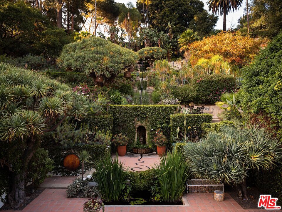Perched above the treetops on one of Los Feliz's most storied streets, is a rare architectural gem a 1922 Spanish estate with major celebrity provenance, set behind gates on nearly 1.5 acres of exquisitely landscaped grounds. A once-in-a-lifetime offering, this grandly scaled and deeply soulful home beautifully balances preserved period detail with refined interior updates by Los Angeles-based design studio, Commune Design. Inside, soaring original beams and hand-painted ceilings crown a series of awe-inspiring public rooms, each filled with natural light and seamlessly opening to the home's expansive patios and terraces. A glamorous den/media room, richly paneled card room, and en-suite guest bedroom complete the main level. The updated eat-in kitchen, stylishly reimagined, opens to a private outdoor dining patio tucked into the garden. Upstairs, the sunlit primary suite includes a newly renovated period-appropriate bath, generous dressing area, and a balcony overlooking the verdant hillside. A second upstairs suite, also with a newer bath, enjoys tranquil garden views. The resort-like grounds are a world of their own, with a freeform pool, cold plunge, amphitheater, outdoor fireplace, scenic fire pit, and meandering water features cascading toward a koi pond. Multiple patios, flat pads, and hidden garden paths invite entertaining or quiet retreat, all surrounded by lush plantings and sweeping views that stretch across the city. Rich in character, history, and magic, 2666 Aberdeen Avenue is a truly exceptional Los Feliz estate timeless, transportive, and unforgettable.