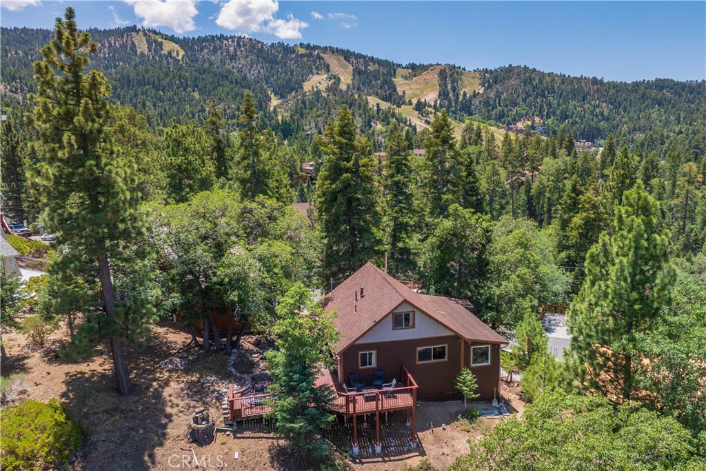 Gorgeous, forested tree-top views frame this wonderful Moonridge retreat creating an exceptional base for mountain living and year-round adventure! Experience fantastic sunsets on the expansive rear wood deck that invites outdoor dining and relaxed evenings gathering around the fire pit under star-filled skies. Surrounded by trees and peaceful scenery, it’s a true extension of the home’s tranquil setting. The Great Room delivers a wonderful first impression with a beautiful stone fireplace with wood stove insert and large windows that bathe the space in bright, natural light including a picture window with lovely ski-slope views. Rustic wood-beam ceilings, wood-style floors and arched openings add warmth and character throughout. The open-concept kitchen and dining areas flow from the main living area, offering a welcoming space to gather and share meals amongst the treed views that frame each window like a natural work of art. A cozy window-side reading nook invites quiet mornings with coffee or a good place to escape into your favorite book. Two main level bedrooms provide comfortable space for owners and guests alike, along with a full bathroom and convenient in-home laundry. Upstairs, a large loft is the third bedroom with room for a play area and is complemented by a second bathroom with a jetted tub- great for relaxing and unwinding after a long day on the slopes. A great additional storage space beneath the home offers a convenient spot to stow mountain gear, seasonal items and tools. Located just minutes from Bear Mountain, Snow Summit, the golf course, zoo, & trails, this fantastic Moonridge location provides wonderful access to outdoor recreation. The lake, markets & Big Bear’s Village with shopping and dining are just a short drive away. Whether you’re looking for a weekend escape, full-time haven or income-producing short-term rental, this fantastic home with stunning views offers many possibilities. Much of the home’s furniture, décor, kitchenware and electronics are available- so you can start enjoying your mountain experience right away.