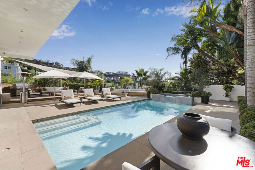 Above Sunset Plaza, this California contemporary welcomes you with a gated approach, a calming water feature, and impressive double doors. Inside, the home opens to dramatic 15-foot ceilings, expansive glass, and sun-filled spaces that open directly to the pool and an expansive outdoor living area, creating a incredible sense of openness. A bright open kitchen, sophisticated wet bar, illuminated Poliform shelving, and a statement marble fireplace anchor the main level, enhancing the home's refined aesthetic and offering an elevated environment for both everyday living and entertaining. The primary suite captures sweeping canyon and city views, providing a serene and private retreat.