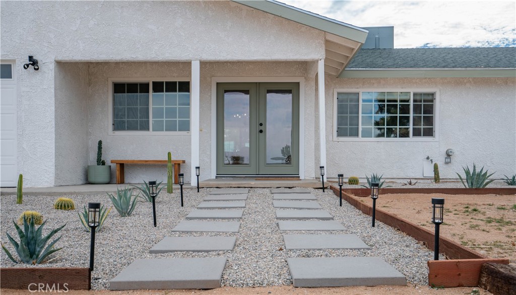 Sitting at the gateway where Yucca Valley meets Joshua Tree, this stunning fully furnished desert ranch home offers the perfect blend of rustic charm and modern upgrades. This 3 bedroom, 2 bath home spans 1,520 sq. ft. on over 2 acres of land, providing both privacy and plenty of space to enjoy the desert lifestyle. Step inside to a welcoming formal living room with new laminate flooring, crown molding, and a cozy wood-burning fireplace. The open-concept kitchen and family room showcase brand-new white shaker cabinets, stone countertops, upgraded stainless steel appliances, and a sliding door leading to a full-length covered back patio—ideal for indoor-outdoor living. Additional highlights include updated dual-pane windows, industrial farmhouse-style fixtures, and modern LED lighting throughout. Bedrooms feature plush new carpet with mirrored wardrobe doors, while the hallway offers a rustic barnwood farmhouse pantry and linen area. The primary suite boasts direct patio access along with an en suite bathroom featuring an updated vanity, fixtures, and tub/shower combo. Comfort is ensured with central HVAC and an evaporative cooler. Along with a 2-car attached garage, the property features two 4-car detached metal garages, offering a total of 10 covered parking spaces. These versatile spaces are perfect for car enthusiasts, off-road vehicle owners, workshops, studios, or creative retreats. Nearly the entire property is fenced with ample space for recreation and additional parking. A custom-built storage shed/playhouse and an abundance of Joshua Trees, Yucca Trees, and native desert landscaping add to the property’s charm.