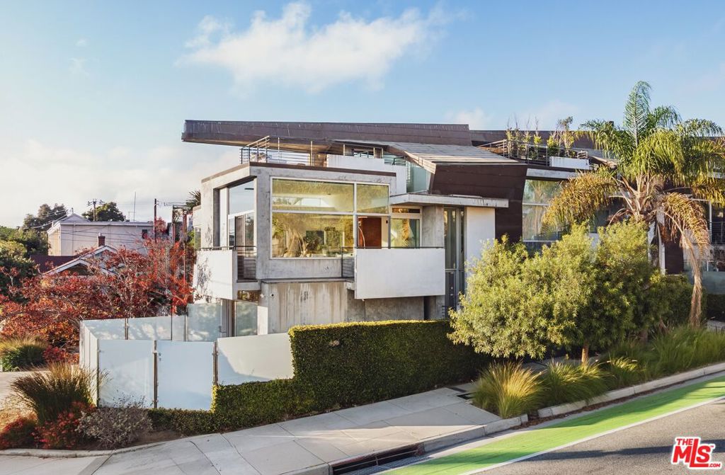 Located in an architecturally significant building in Ocean Park designed by Michael Folonis, this residence sits in one of the Westside's most desirable neighborhoods. Just moments from the ocean, shops, restaurants, and cafes, it offers the perfect balance of relaxed coastal living and urban convenience. Positioned at the front of a rare three-unit building, the home features glass on three sides, filling the interiors with natural light and refreshing ocean breezes. A dramatic three-story atrium and staircase accentuate the sense of openness. Ceiling heights ranging between 8 and 20 feet create an atmosphere that is at once warm and grand, tied together with thoughtful architectural details. The main living area features floor-to-ceiling glass walls with views stretching toward the ocean, complemented by a balcony ideal for enjoying coastal breezes. The open kitchen and dining area are designed for entertaining, finished with Bianco Romana granite stone, custom wood veneer cabinetry, soaring ceilings, and a clerestory window that floods the space with light. A full bathroom on the main level adds convenience for guests. On the lower level, the spacious primary suite offers Claro Walnut wood veneer closets on two sides and direct access to a private patio enclosed in frosted glass for privacy. The ensuite bathroom showcases Italian Statuarieta stone, dual sinks, a frameless glass waterfall shower with dual Dornbracht fixtures, and sleek finishes throughout. Two additional bedrooms, each generously sized, share a full bathroom also finished in Statuarieta stone. One bedroom includes private outdoor space. Above the main living level, a mezzanine provides the perfect home office or lounge, leading to a private rooftop deck with treetop, neighborhood, and ocean views. This is an exceptional space for year-round entertaining. Additional features include in-unit laundry, secure private access, and two side-by-side parking spaces in a gated underground garage. This is a rare opportunity to live in an architecturally significant residence in the heart of Santa Monica, designed for the most discerning buyer.
