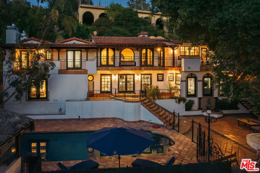 Nestled into Glendale's coveted Royal Canyon neighborhood is a one-of-a-kind estate, the kind of truly special property where every corner is rich with history and heart. 1664 Las Flores Drive is not just a house -- it's a love letter to old-world elegance and timeless Hollywood glamour. From the moment you pass through the front gates, you're transported. A private front hacienda welcomes you to a 1935 Spanish colonial home set off with dramatic arches, colorful tilework, and a stunning cupola with weathervane. The formal living room features massive windows that bathe the home in natural sunlight - incredible at golden hour - as well as beamed ceilings and a beautifully tiled fireplace (one of four). The kitchen is a home chef's dream, with walk-in pantry, ample storage space, massive island with built-in wine refrigerator, dedicated dining space, spacious balcony, and skylights that offer expansive views of the elegant oaks and hills beyond. The top floor boasts two bedrooms and two bathrooms, one of which features picture windows with incredible views, a stunning tiled fireplace, and an ensuite bath - a perfect guest suite or second primary. Downstairs, find a spacious second living/family room with Saltillo tile floors and gorgeous wood sliding doors out to the yard - the ideal place to unwind and spend time relaxing with loved ones. On one side of the stairway is a third bedroom as well as bonus office/study/creative space or extra (fifth) bedroom. On the other, find yourself in an elegant primary suite with fireplace, dual walk-in closets, and a dreamy bathroom with jetted soaking tub and separate shower. But the magic doesn't stop indoors - out back, find yourself in an entertainer's paradise, a celebration of California living at its finest. The sparkling pool, surrounded by lush, mature landscaping, feels like a tropical vacation retreat. Enjoy drinks and dining al fresco in the spacious cabana with built-in kitchen, or shoot some hoops from the lower terrace while taking in the stunning facade of the west side of the house - wrought iron, bougainvillea, and breathtaking Spanish tile that catches the sun as it dips behind the hills. At the back of the property, find an oversized detached garage that's accessible from a separate road. Located in the sought-after Glendale Unified school district and moments away from hot spots in Glendale and Northeast LA, you're close to the best of city life while tucked away in your own private sanctuary. 1664 Las Flores Drive is truly the rarest of gems: an estate for those who crave the kind of timeless beauty and resort-style living that never goes out of style.