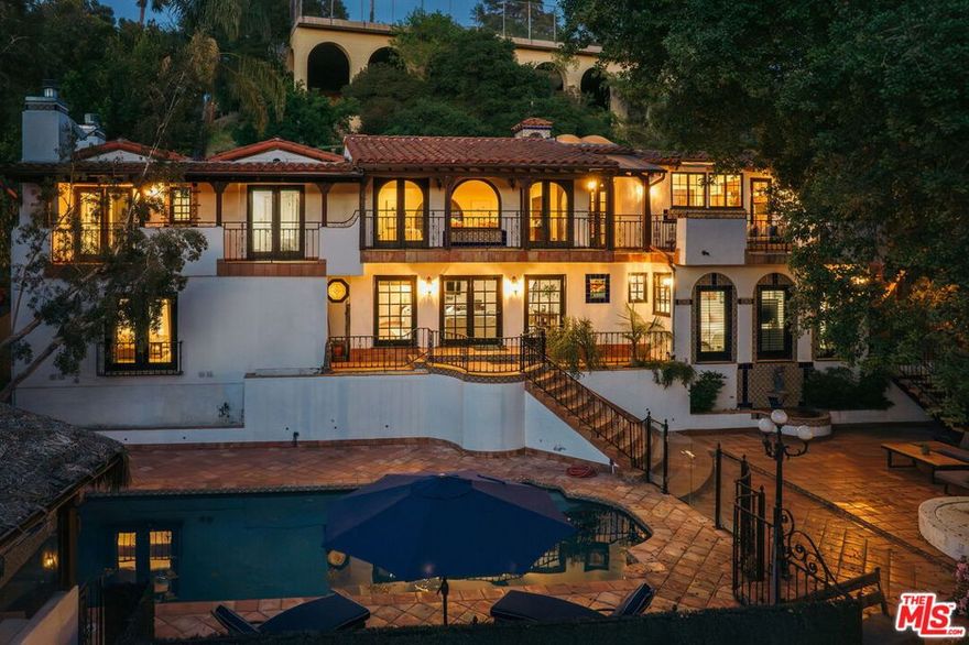 Nestled into Glendale's coveted Royal Canyon neighborhood is a one-of-a-kind estate, the kind of truly special property where every corner is rich with history and heart. 1664 Las Flores Drive is not just a house -- it's a love letter to old-world elegance and timeless Hollywood glamour. From the moment you pass through the front gates, you're transported. A private front hacienda welcomes you to a 1935 Spanish colonial home set off with dramatic arches, colorful tilework, and a stunning cupola with weathervane. The formal living room features massive windows that bathe the home in natural sunlight - incredible at golden hour - as well as beamed ceilings and a beautifully tiled fireplace (one of four). The kitchen is a home chef's dream, with walk-in pantry, ample storage space, massive island with built-in wine refrigerator, dedicated dining space, spacious balcony, and skylights that offer expansive views of the elegant oaks and hills beyond. The top floor boasts two bedrooms and two bathrooms, one of which features picture windows with incredible views, a stunning tiled fireplace, and an ensuite bath - a perfect guest suite or second primary. Downstairs, find a spacious second living/family room with Saltillo tile floors and gorgeous wood sliding doors out to the yard - the ideal place to unwind and spend time relaxing with loved ones. On one side of the stairway is a third bedroom as well as bonus office/study/creative space or extra (fifth) bedroom. On the other, find yourself in an elegant primary suite with fireplace, dual walk-in closets, and a dreamy bathroom with jetted soaking tub and separate shower. But the magic doesn't stop indoors - out back, find yourself in an entertainer's paradise, a celebration of California living at its finest. The sparkling pool, surrounded by lush, mature landscaping, feels like a tropical vacation retreat. Enjoy drinks and dining al fresco in the spacious cabana with built-in kitchen, or shoot some hoops from the lower terrace while taking in the stunning facade of the west side of the house - wrought iron, bougainvillea, and breathtaking Spanish tile that catches the sun as it dips behind the hills. At the back of the property, find an oversized detached garage that's accessible from a separate road. Located in the sought-after Glendale Unified school district and moments away from hot spots in Glendale and Northeast LA, you're close to the best of city life while tucked away in your own private sanctuary. 1664 Las Flores Drive is truly the rarest of gems: an estate for those who crave the kind of timeless beauty and resort-style living that never goes out of style.