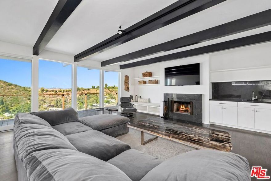 Presenting a newly renovated view home in Beverly Hills Post Office, sited at the end of a long private cul-de-sac drive with 180-degree panoramas of the canyon, mountains, city, and ocean, from Palos Verdes to Catalina Island. Experience striking vistas from the large Brazilian Ipe viewing deck spanning the entire width of the home, accessed by both the primary suite and living room, with its floor-to-ceiling picture windows, sleek exposed beams, wood-burning fireplace, wet bar, and built-in reading nook. Rich wood floors flow into the bright kitchen with marble countertops, breakfast bar, recipe station, and stainless-steel appliances including Wolf range with hood. The owner's bedroom is a serene and relaxing retreat, complete with en-suite spa-inspired bath with beautiful stone work, oversized full-slab steam and rainwater shower with bench, and smart toilet. The light-filled secondary bedroom and bathroom are also smartly appointed with modern finishes, including a modern two-person whirlpool tub. Entertain guests, dine al-fresco, and gather around the fire pit under California skies in the expansive open-air patio, concealed and gated from the street. For convenience, there is a one-car garage plus carport with 30-amp plug for EV fast-charging capability as well as low-maintenance, drought-tolerant landscaping. The home is also wired for high-speed fiber optic internet from AT&T. Originally built by Stone-Fisher, highly regarded architects of the time, the home was extensively remodeled in 2023. Welcome to this excellent central location, tucked away from the city yet just moments to the high fashion of Rodeo Drive, the Sunset Strip, Century City, and the greater Westside. The Valley and Hollywood studios are also just a quick canyon drive away.