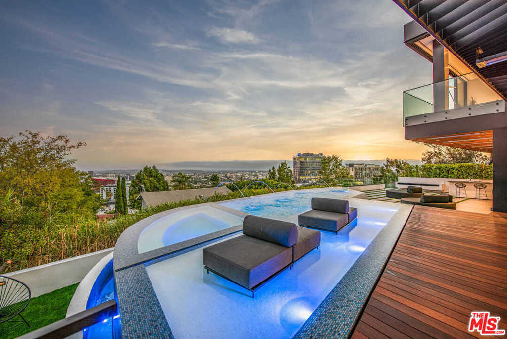 Perched atop the Sunset Strip, this warm, contemporary residence, designed by world-renowned architect Hagy Belzberg offers the amenities and experience of a luxury resort - a true tranquil paradise of architectural significance. Featuring one of the first digital NFT art home installations and equipped with a temperature-controlled glass wine cellar, dual kitchens, 2 outdoor bars, Crestron home automation, Sonos sound, 4-sided infinity edge pool and fire pit overlooking panoramic views. Other notable details include motorized sliding glass walls, striking runway-style driveway 30-feet above the street, motor court with turntable, air-conditioned 3-car garage, along with a 24-foot glass water feature that cascades down all 3 floors. The lower level is a sultry and polished private speakeasy with dark leather and walnut-paneled walls, movie theater and stunning bar area. The 4 ensuite bedrooms upstairs are punctuated with amazing views from DTLA to the ocean. Enjoy proximity to fine dining and shopping.
