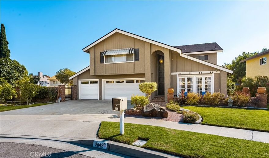 Located in the beautiful City of Orange, this wonderful, multi-generational home, or beautiful home with multiple options, is located at the end of a cul-de-sac beautifully landscaped with roses and cottage garden flowers, and separated by the large three-car driveway is a cute little orchard area with beautiful grapevines, apple trees, papaya, plum, and fig trees. The front yard has a beautiful used-brick courtyard and low fencing, making the grounds charming. The house is approximately 2,700 square feet and includes a large three-car attached garage with three parking spaces and a double-door (looking) entrance opening to the foyer, which has a staircase to the upstairs and a separate entrance to the main living area. As you enter into the main living area, you are welcomed into the charming family room with one of two beautiful fireplaces and open to the country kitchen with newer stainless steel appliances and a farm sink, overlooking the covered back patio and pool area that is ready to be landscaped as beautifully as the front yard. Access from the kitchen leads to the beautiful dining room and living room with high cathedral ceilings and double French doors leading to the front courtyard. Your laundry, full bath, and 4th bedroom are also in the downstairs area, as is access to your three-car garage. Upstairs, there is a beautiful grand suite with its own fireplace, upgraded mirrored wardrobe closet, and a full bath consisting of a separate double sink, vanity area, and walk-in closet, as well as a separate bath, shower, and toilet area. This beautiful suite is extremely large and feels even larger with its cathedral ceilings. The second kitchen, complete with its own laundry, is also on the second floor, as is another full bath, a large bedroom with triple mirrored wardrobe closet doors, and finally a large room, currently being used as another private suite with high cathedral ceilings. All bedroom and bathroom doors have been upgraded, along with other lovely improvements made through the years. This home gives you many options for how to enjoy it and is conveniently located near UCI Medical Center, CHOC, St. Joseph Hospital, Chapman University, and is freeway close to major connections. Angel Stadium, the Honda Center, and Disneyland are also nearby, adding to the incredible convenience and appeal of this beautiful Orange home.