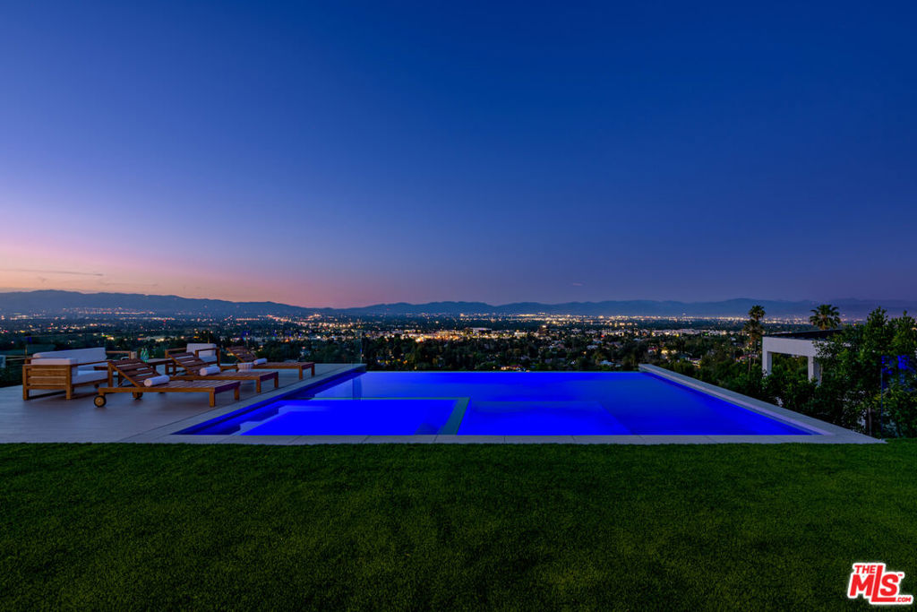 A one-of-a-kind masterpiece where striking design meets awe-inspiring vistas - welcome to your elevated sanctuary above it all. Perched on a tranquil, wide street, this newly completed 2025 estate captures breathtaking, unobstructed views unlike anything else on the market - a visual masterpiece that stretches endlessly across the Valley, painting a living canvas of city lights, rolling hills, and golden sunsets. Every inch of this contemporary showpiece has been meticulously crafted to frame and celebrate the views, from the expansive floor-to-ceiling glass walls to the ultra-wide pocket doors that vanish completely, erasing the line between indoors and out. The result? A seamless flow into your private outdoor paradise where an infinity-edge plunge pool appears to spill into the skyline, and every moment is backdropped by nature's finest work. Inside, soaring 11-foot ceilings and rich, wide-plank oak floors complement the open, airy layout. The living room, dining area, and chef's kitchen form a sunlit great room that is at once grand and intimate, all oriented to maximize the unparalleled scenery. The kitchen is a dream for entertainers and culinary enthusiasts alike, with bespoke cabinetry, a custom oversized island, and top-of-the-line Thermador appliances. The primary suite is a retreat of rare caliber - elevated and private with jaw-dropping views from both the bedroom and spa-like bathroom, where dual showers and a sculptural soaking tub invite you to unwind. Incredible view balconies extend the experience even further, offering intimate spaces to take in the surrounding beauty. You will never enjoy a hotel in the same manner because this home will make you feel like you are downgrading when traveling. Beyond its five bedrooms and six baths, this home is loaded with lifestyle-enhancing luxuries: a dramatic three-level theater, a home office, gym, a dry sauna, bespoke bar and billiards lounge - all designed with both comfort and wow-factor in mind. This is not just a home - it's an experience. A singular offering where every detail is elevated by some of the most extraordinary views Los Angeles has to offer. Step in, and look out - you've never seen anything like it.
