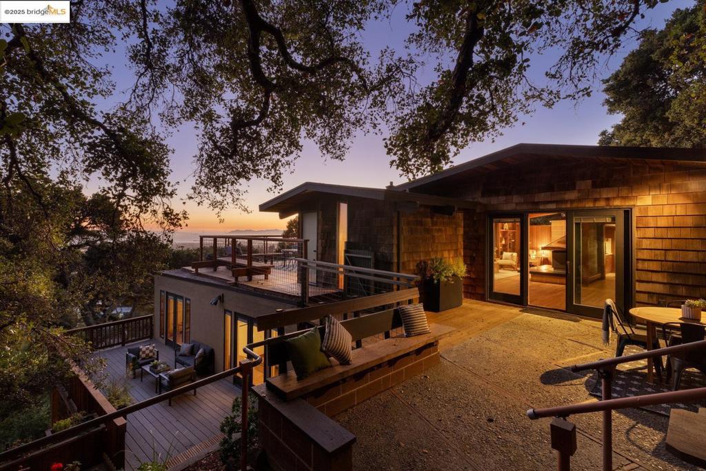 Designed by renowned Bay Area architects Ratcliff and associates, this mid-century residence was envisioned to frame the dramatic natural beauty of Berkeley. Expansive west-facing windows and tiered decks showcase views of the nearby UC Camponile, the Bay, San Francisco, the Golden Gate, and the Marin Headlands, infusing the home with light and ever-changing sunsets. Inside, the architecture is defined by redwood vaulted beam ceilings, rough-sawn cedar paneling, and angular, elongated windows, which channel the era’s hallmark simplicity and warm artistry. Thoughtful craftsmanship throughout features a copper-hooded gas fireplace anchoring the living room, and a custom stained-glass door commissioned from a local Berkeley artist. The home’s generous floor plan offers 3 bedrooms, 2 full bathrooms, 2 half bathrooms, with a home office suite with its own bath and laundry, a wine cellar, and bonus spaces designed for both creativity and entertaining. A 1980s addition introduced a flexible wing with a family room/ office with a wet bar, separate entrance, and a professional darkroom, workshop, and an excess of storage, enhancing the home’s versatility for modern living. Outdoors, the property unfolds across more than 11,000 sq ft of gardens, patios, decks, and a hot tub