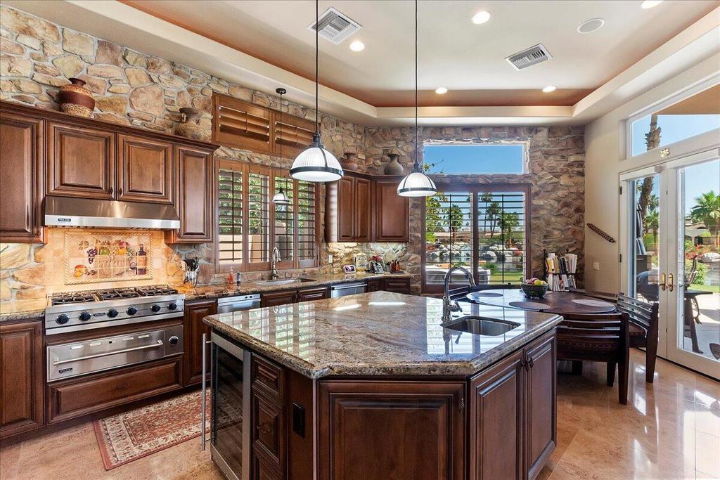 Discover timeless elegance and unmatched comfort in this fully furnished 4,500 sq ft custom estate, ideally located in the heart of PGA West's exclusive Stadium development. Situated on a generous 15,682 sq ft corner lot with panoramic lake views, this property combines sophistication and serenity in one breathtaking package. From the moment you arrive, the curb appeal is undeniable--stone front exterior, circular paver driveway, and an expansive front patio set the stage. Enter through a designer metal-and-glass front door into a world of refined finishes, including travertine flooring, custom Alderwood cabinetry throughout, and plantation shutters. The open-concept layout flows beautifully, anchored by a chef's kitchen featuring bullnose granite countertops, Viking appliances, a wine cooler, walk-in pantry, and a large island ideal for casual dining or entertaining. The step-down wet bar enhances the entertaining experience, while the living room fireplace and surround sound media room make every moment feel intentional. The formal dining room invites celebration, and the attached private-entry casita with its own living room is perfect for guests or in-laws. The primary suite offers its own fireplace, luxurious en-suite bath, and direct outdoor access. Speaking of outdoors--you'll enjoy a backyard oasis with a custom outdoor kitchen, fireplace, raised spa, and sparkling pool, all framed by mature landscaping and lakefront tranquility. Garage parking for three cars, plus a golf card. This is more than just a home--it's a statement of lifestyle, comfort, and class in one of La Quinta's most coveted neighborhoods.