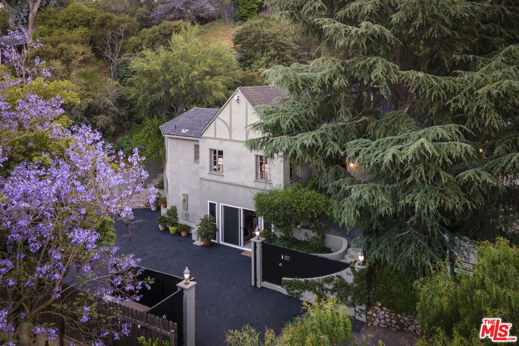 Tucked away in the coveted Laurel Canyon enclave, this timeless 1920s Tudor estate blends old Hollywood glamour with contemporary comfort. Sitting on a sprawling half-acre lot, this gated home boasts rare six-car parking and a perfect mix of privacy and style. Inside, dramatic coved ceilings and a cozy wood-burning fireplace set the tone, enhanced by warm natural light streaming through every room. French doors open to a magical backyard retreat where lush greenery, fruit trees, and vibrant gardens surround a sparkling pool and spa. Whether you're enjoying dinner under the stars, gathering around the fire pit, or hosting at the outdoor buffet bar, every space invites relaxed luxury. Follow the stone steps up to an expansive turf yard with lounge area and then continue up to find a peaceful yoga and meditation level with stunning views of the hills and the Hollywood sign. Back inside the main level, the heart of the home features a spacious family room flowing into a chef's kitchen with a breakfast bar ideal for entertaining or easy everyday living. The private bedroom wing includes a sunlit primary suite with walk-in closet and spa-like bath, complete with clawfoot tub and double vanities. Two additional bedrooms share a beautifully updated bathroom, making the layout ideal for families or guests. Need more space? A generous bonus level downstairs offers flexibility for a studio, office, or guest suite with its own bath. All of this in the highly sought-after Wonderland School district. This reimagined estate is more than a home, it's your own slice of California paradise.