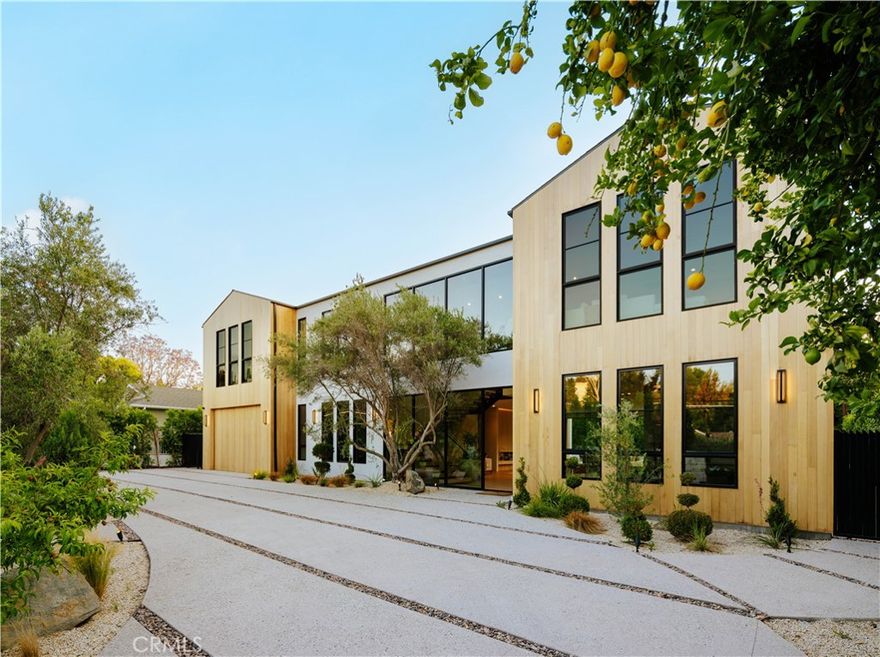 Set behind gates on a rare, over 18,000 sqft flat lot, this brand-new Organic Modern estate blends clean architectural lines with warm, natural materials for a sophisticated yet grounded living experience. A striking cedar wood façade is centered around a 125-year-old olive tree, leading to a dramatic glass entry and a two-story foyer with wide-plank European oak floors. The open floor plan flows effortlessly from a formal dining area with a built-in buffet into a chef’s kitchen, featuring custom cabinetry, limestone countertops, Miele appliances, and a large walk-in pantry. A limestone island anchors the space, perfect for entertaining. The family room features a travertine fireplace and walls of pocketing glass doors that open to a resort-style yard with pool and spa all wrapped in natural travertine, tanning ledges, a built-in BBQ, sports court, and a cabana with full bath. The main level includes an ensuite guest room, a bold powder room, a velvet-wrapped media room with blackout drapes, and a glass-enclosed home office. Upstairs, the primary suite impresses with wood-beamed ceilings, travertine fireplace, private balcony, massive walk-in closet, and a spa bath with floor-to-ceiling travertine, soaking tub, dual vanities, and rain shower. Additional highlights include a 2-car garage, Control4 smart system, full home security, and organic, designer-selected finishes throughout. Ideally located minutes from Ventura Blvd, this estate offers a rare blend of modern luxury and natural serenity.