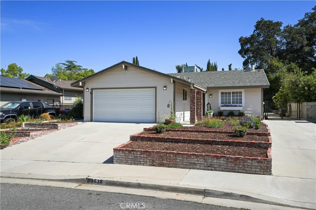 Welcome to this exquisite single-story residence nestled in the highly sought-after Happy Valley community of Newhall. This beautifully appointed home showcases an abundance of natural light, rich wood flooring, and a spacious living room anchored by a charming brick fireplace and crown molding. The open-concept kitchen features stainless steel appliances, a generous walk-in pantry, and flows seamlessly into an arched entry into the formal dining area (previously a bedroom) adorned with a classic chandelier and ample storage, including a stylish coffee bar. The cozy family room offers yet another space for entertaining and gathering.
This expanded stunner offers the versatility of 2 primary suites. The luxurious main suite boasts French doors leading to the backyard, a large in-room flex space, ceiling fan, and a spa-inspired en-suite bath complete with dual vanities, a soaking tub, a separate walk-in shower, and a large walk-in closet. With its own kitchenette, this offers a perfect opportunity for extended family, visitors, or potential rental income. The home also features two more bedrooms (one being the original en suite primary) and a hall bathroom complete with updated vanity and standing shower tub.
Situated on a generous lot, this property boasts a long driveway plus a separate RV-friendly driveway, ideal for additional vehicles or recreational toys. The large entertainer’s backyard offers the perfect setting for gatherings or serene relaxation with its elevated garden area, and plenty of room to create the oasis you’ve always dreamed of.
Located just minutes from shopping, dining, top-rated schools, parks, and convenient freeway access, this home truly offers the best of comfort, style, and location. Don’t miss your chance to call this Happy Valley gem your own!